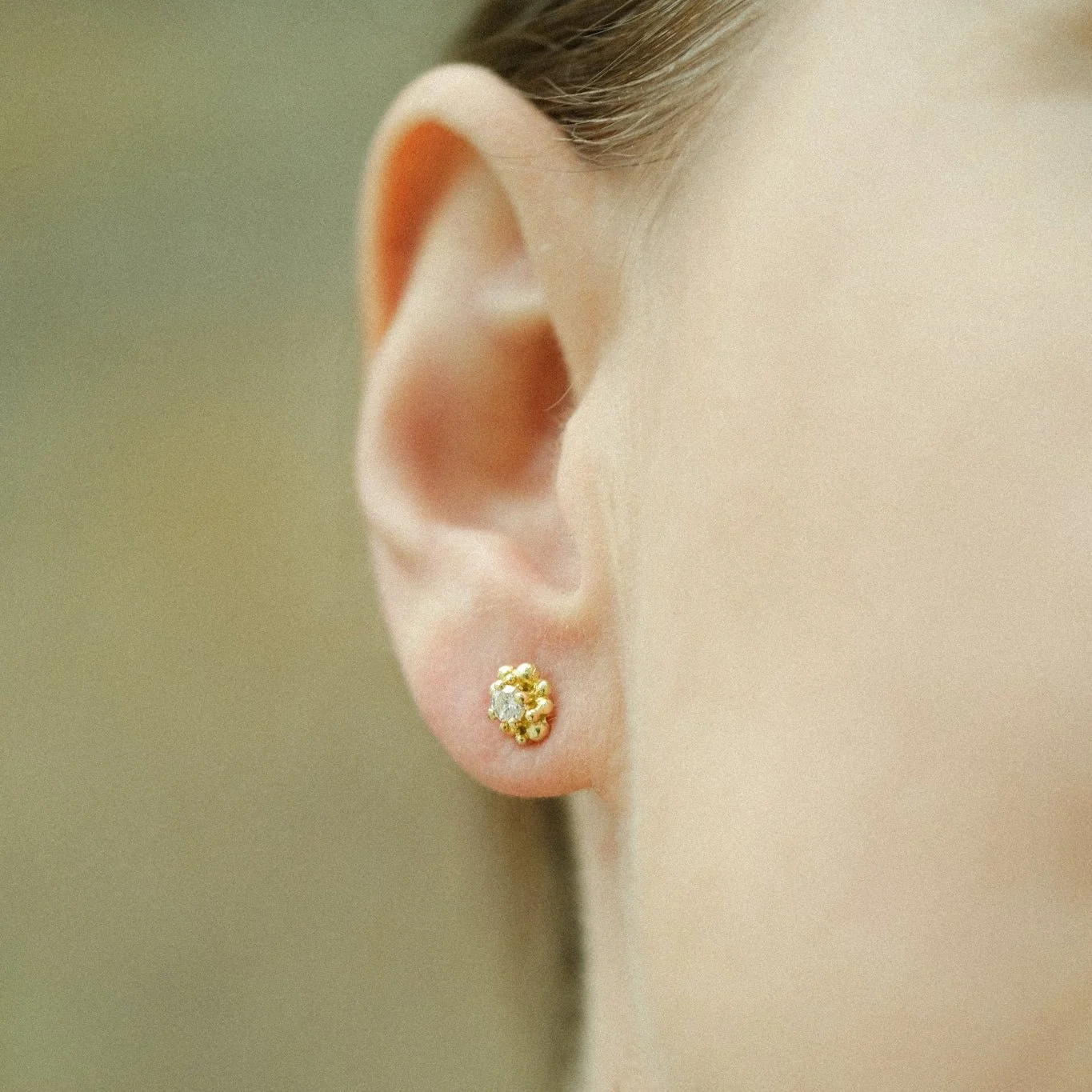 Close-up of a person’s ear with a small gold and diamond stud earring.