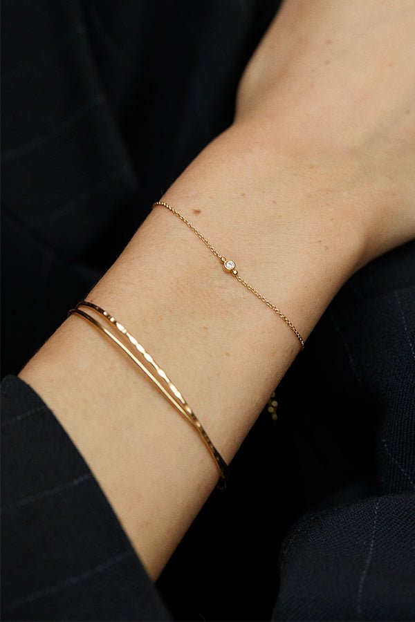 Close-up of a person's wrist adorned with a delicate gold chain bracelet with a small gemstone and two thin gold bangles.