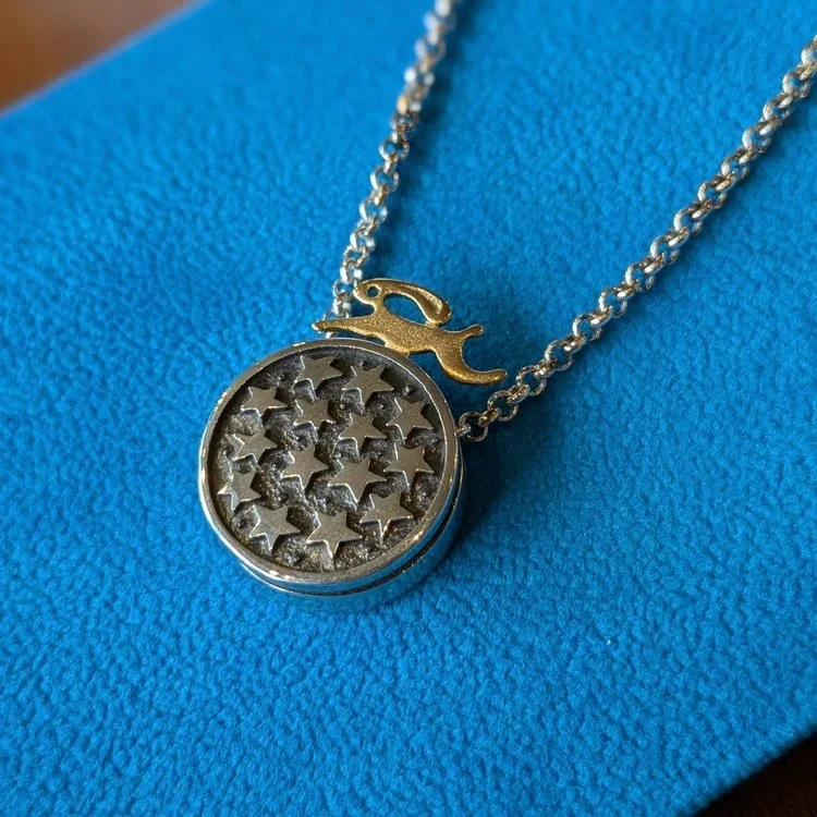 A necklace with a round pendant filled with small stars and a golf club charm, resting on a blue textured surface.