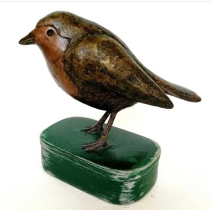 Wooden bird sculpture with painted details on a green oval base.