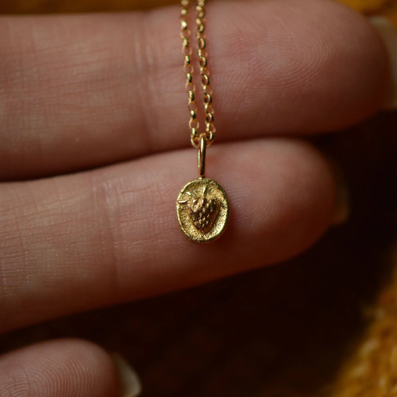 Gold necklace with pendant featuring a strawberry design, held by a person's fingers.