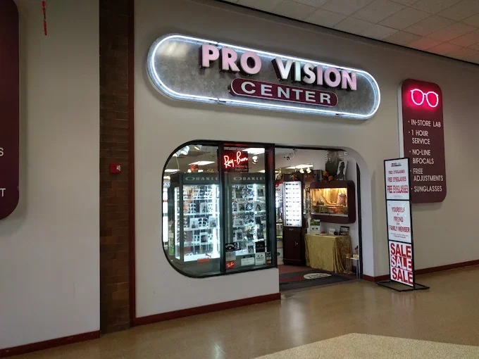 Entrance to Pro Vision Center with neon sign, eyeglasses display, and sale signs outside
