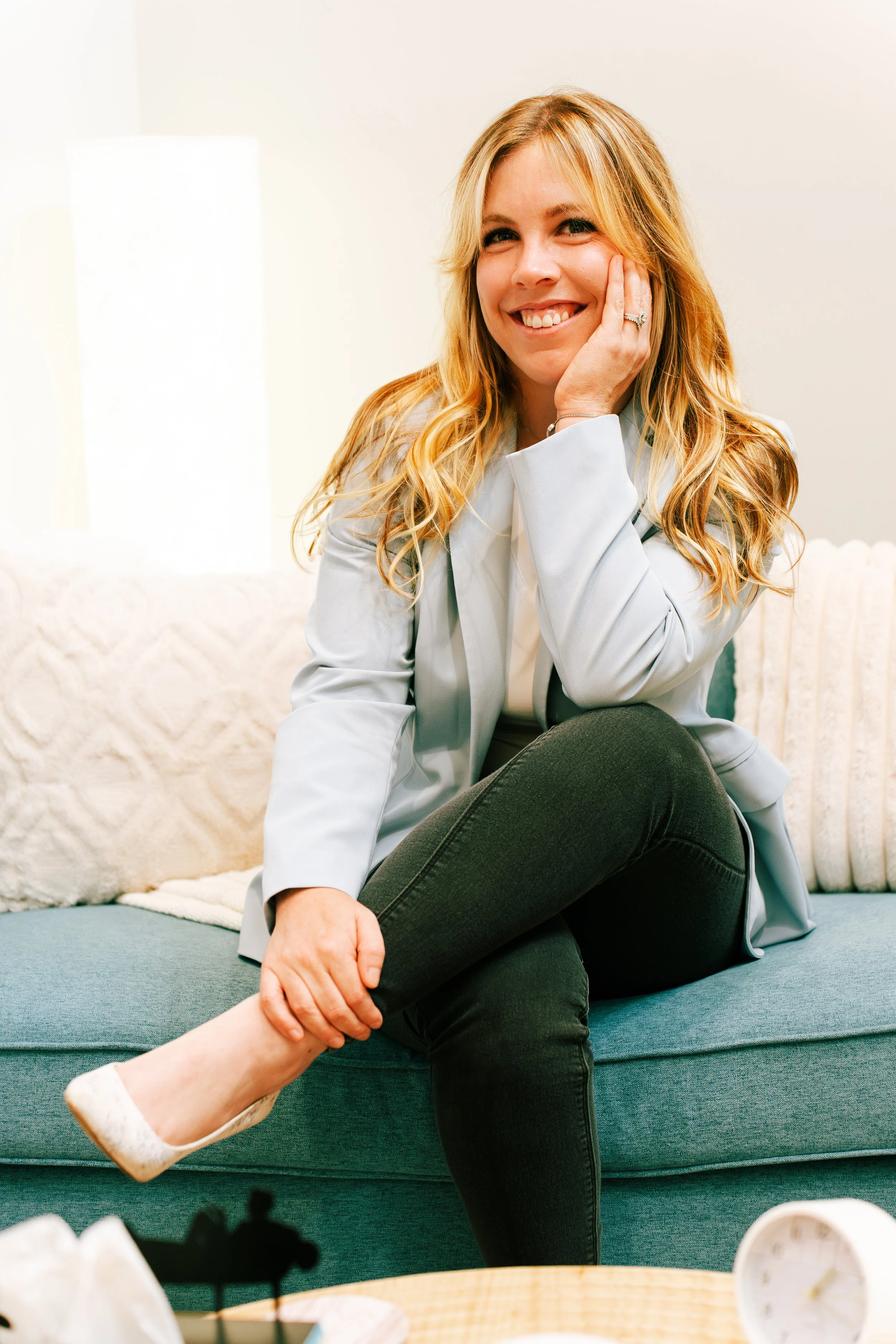 Blonde therapist sits on couch and smiles.
