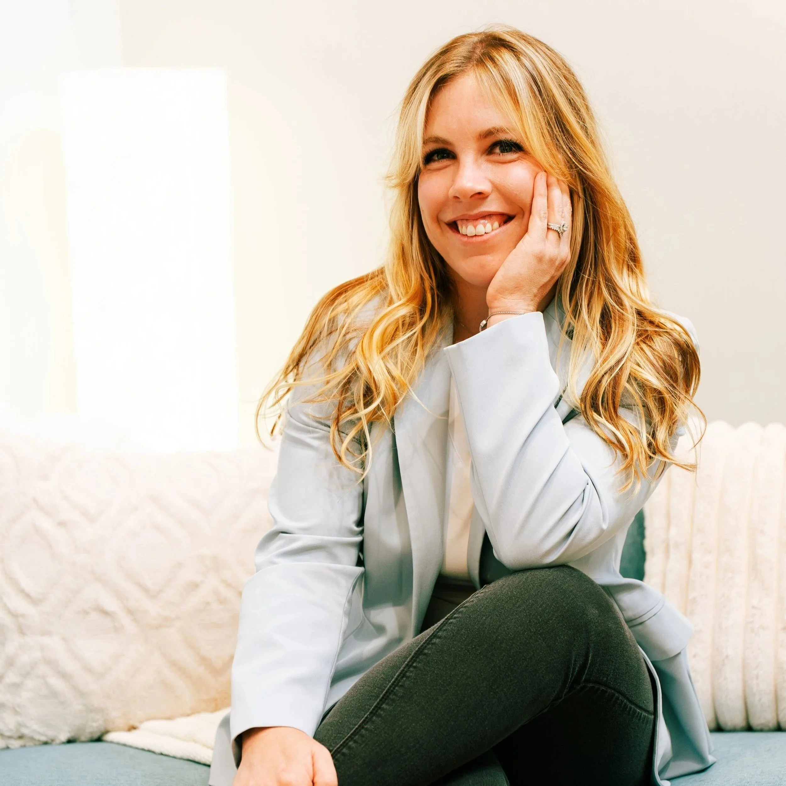 Blonde therapist sits on couch and smiles.