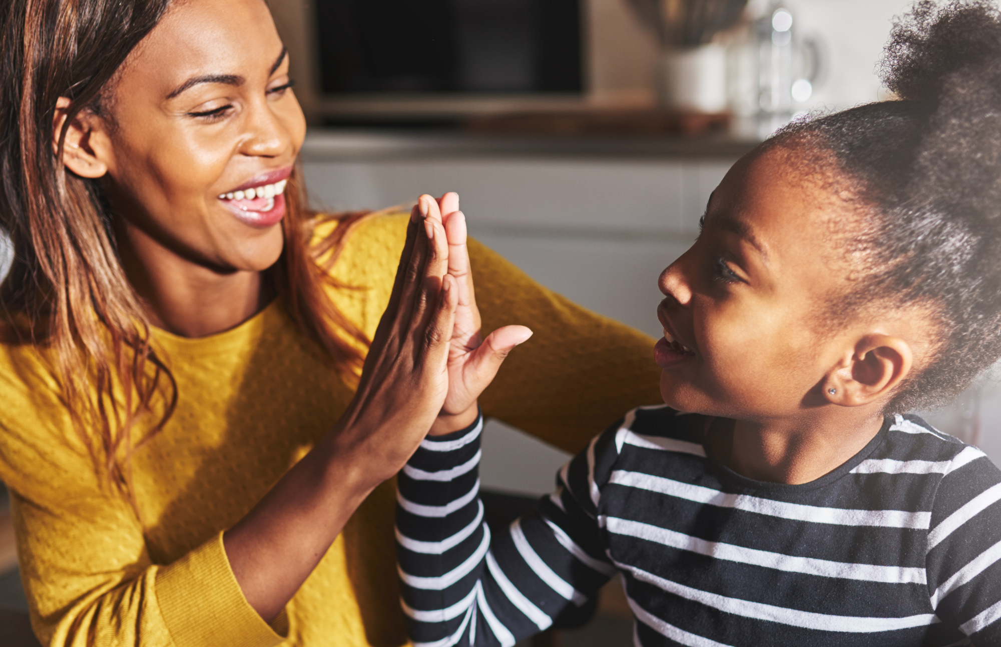 A woman and a young girl high-fiving each other and smiling in a cozy home setting.