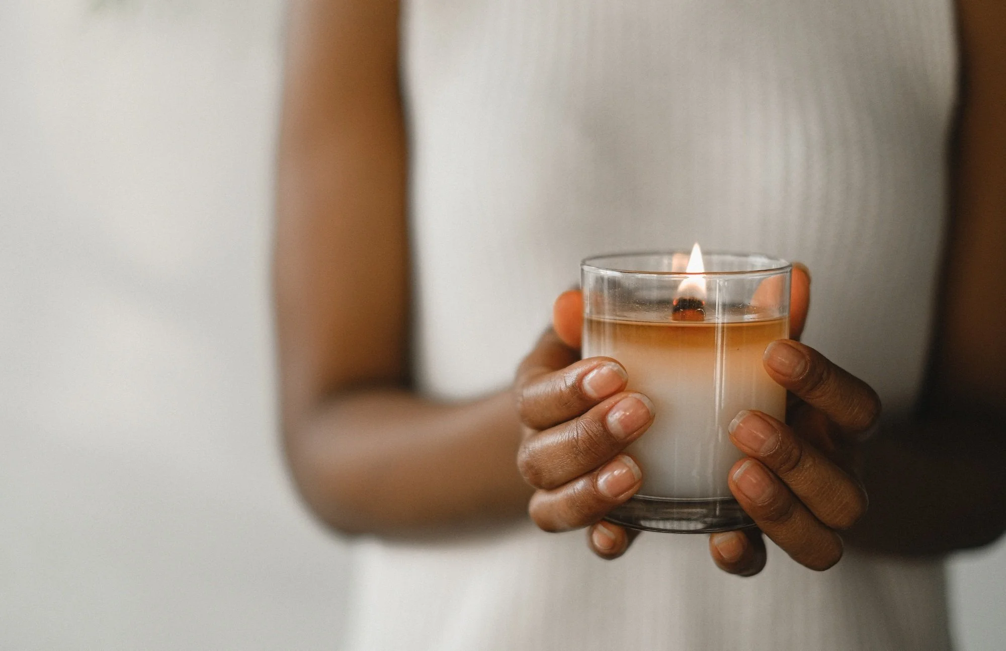 Person holding a lit candle in a glass container.