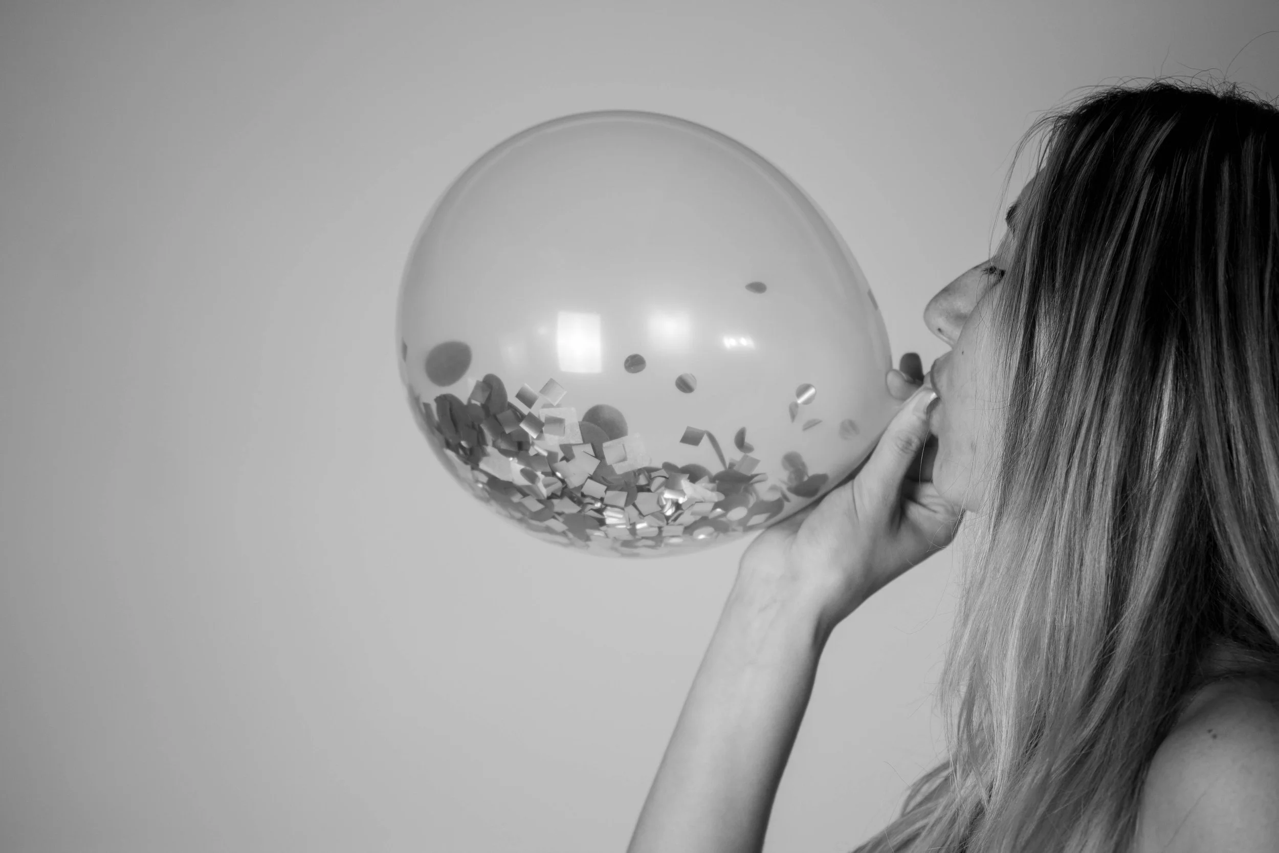 A woman with long hair blowing up a balloon with confetti inside.