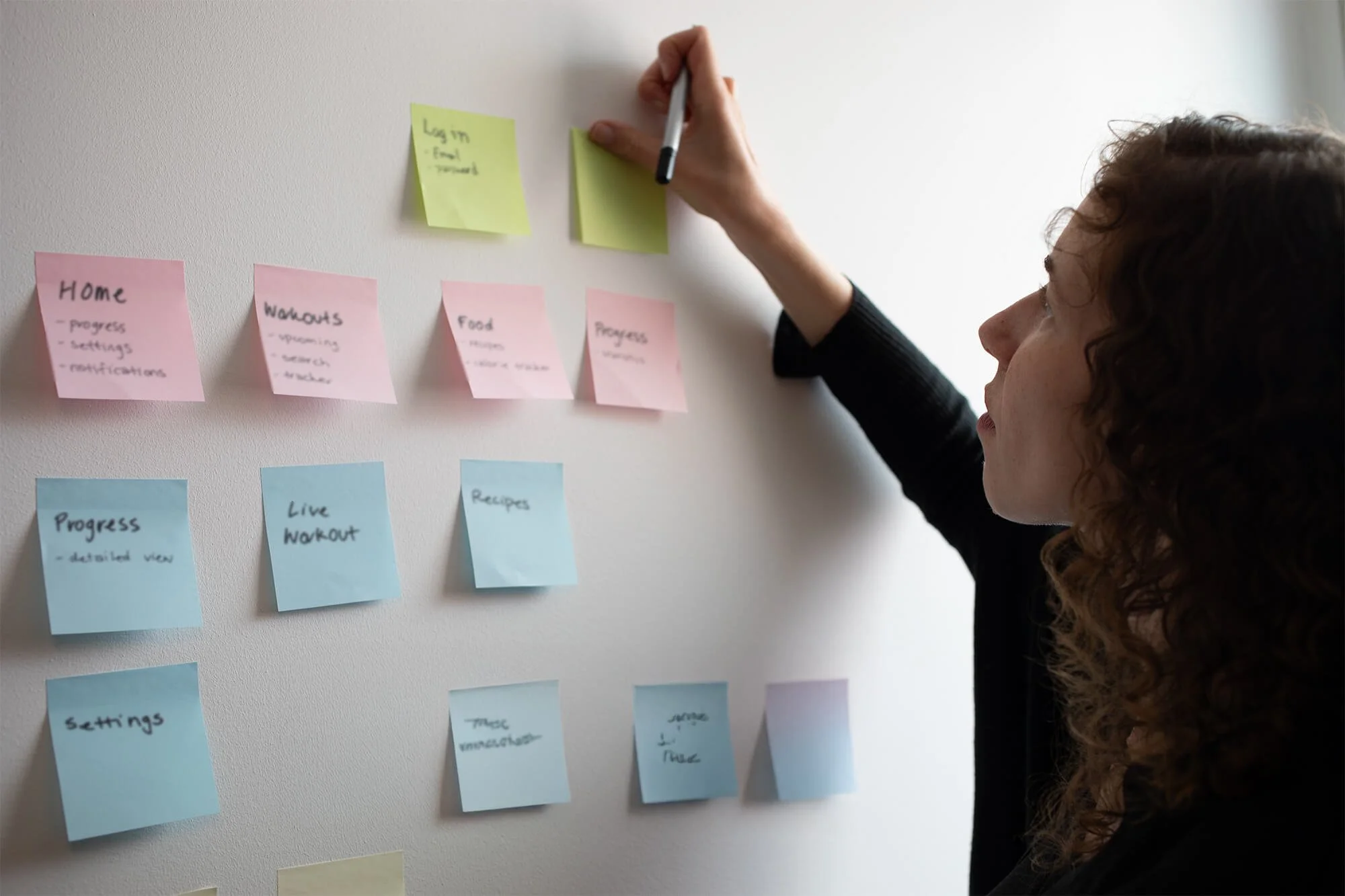 A person places post-it notes on a wall to organize a project.