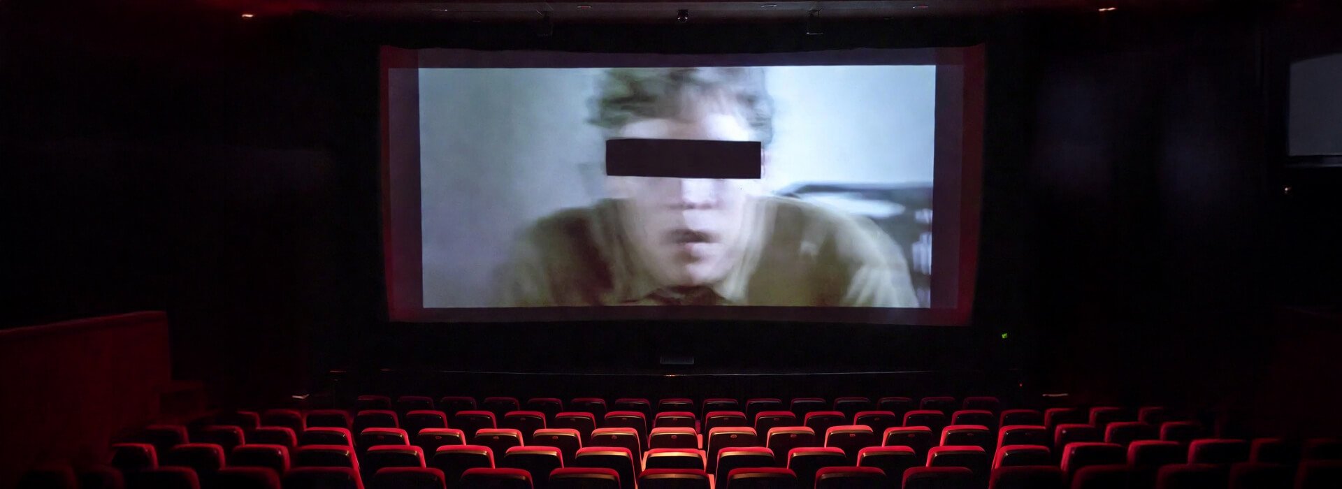A cinema screen showing a film frame with a black censor bar across the face
