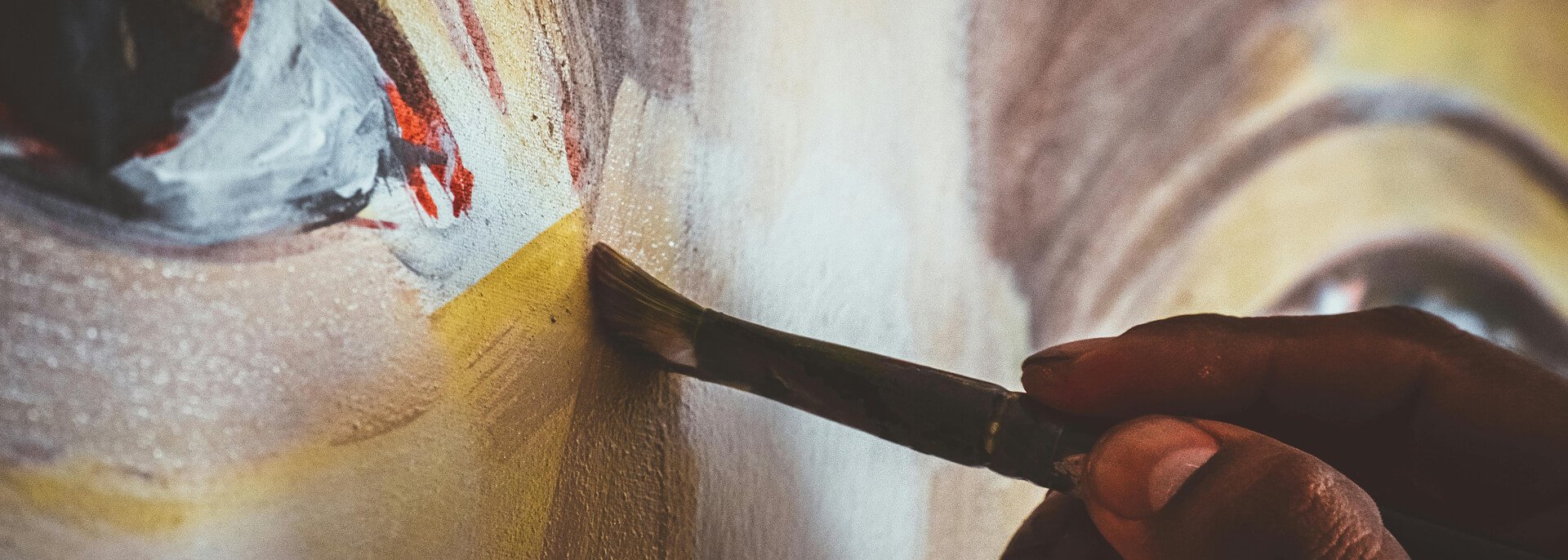 Close-up of an artist using a paintbrush to apply paint onto a textured canvas.