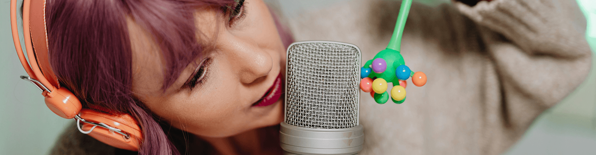 Woman recording ASMR content with headphones on, gently holding a colourful pipe cleaner object near a microphone to create soft tapping and crinkling triggers for relaxing sensory videos
