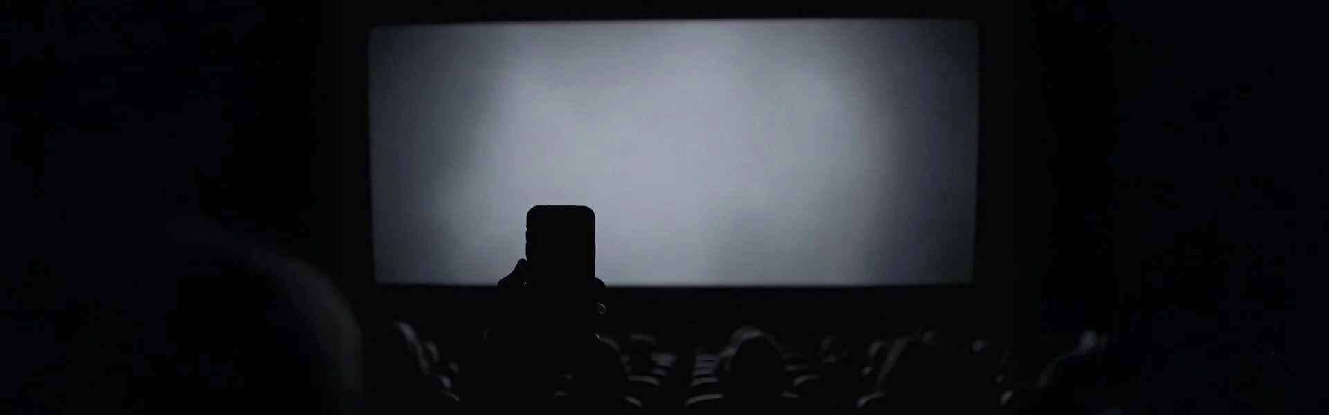 Silhouette of a smartphone held up in a dark cinema, recording the glowing movie screen, symbolizing the start of leaks where altered clips spread faster than original context