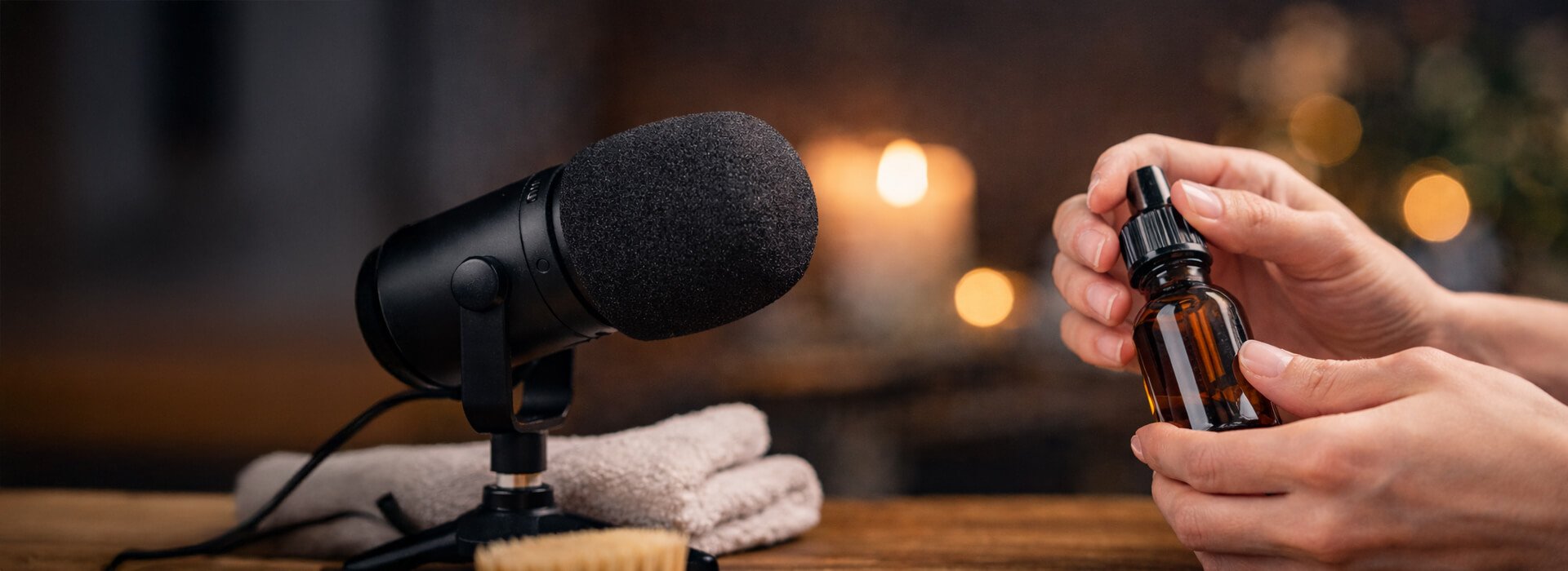 ASMR style close up of hands opening a small amber bottle beside a studio microphone
