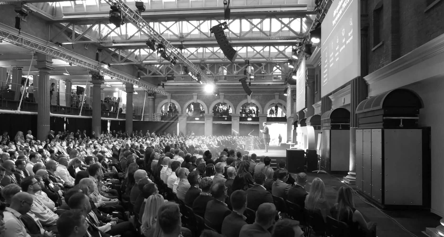 A large conference or seminar with an audience seated and a speaker on stage in a historic-style hall.