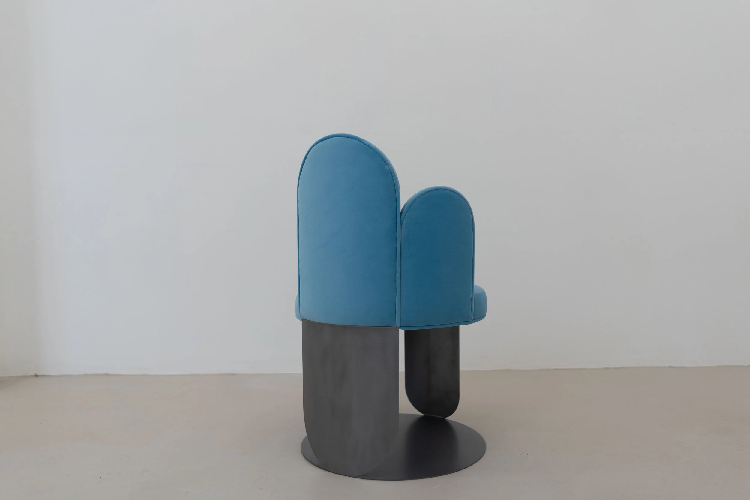 Modern blue and black chair with rounded backrests against a light gray wall.