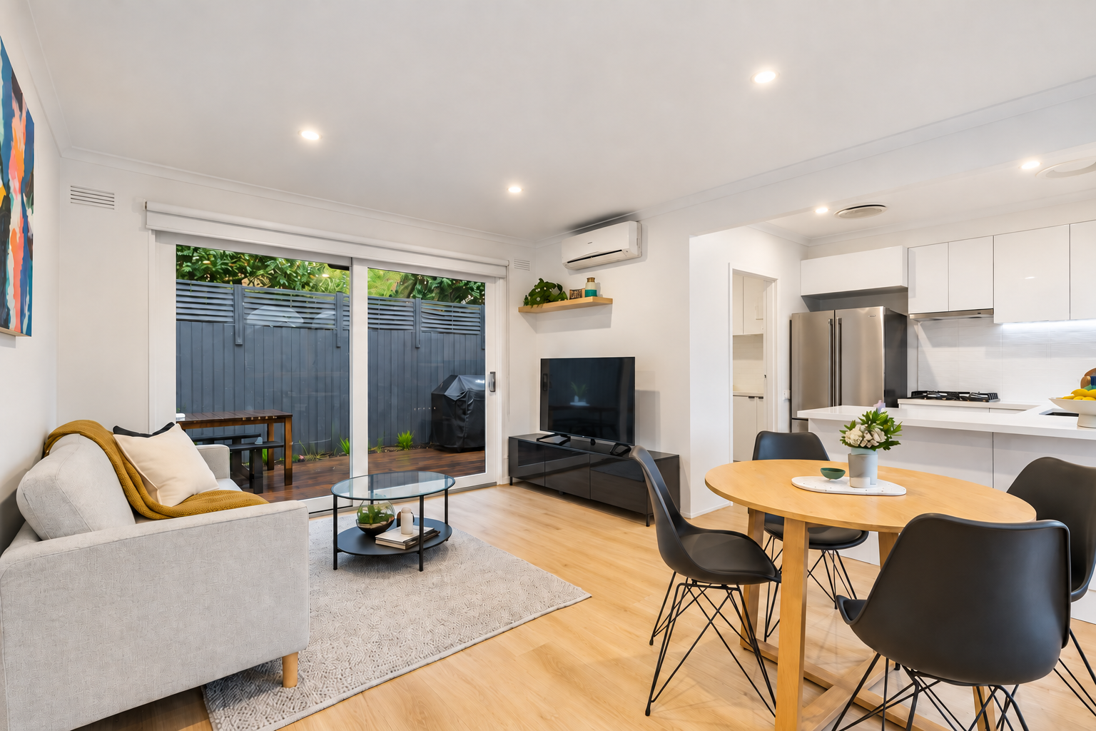 Centre project open-plan living and dining with grey sofa, round dining table and sliding doors to the courtyard