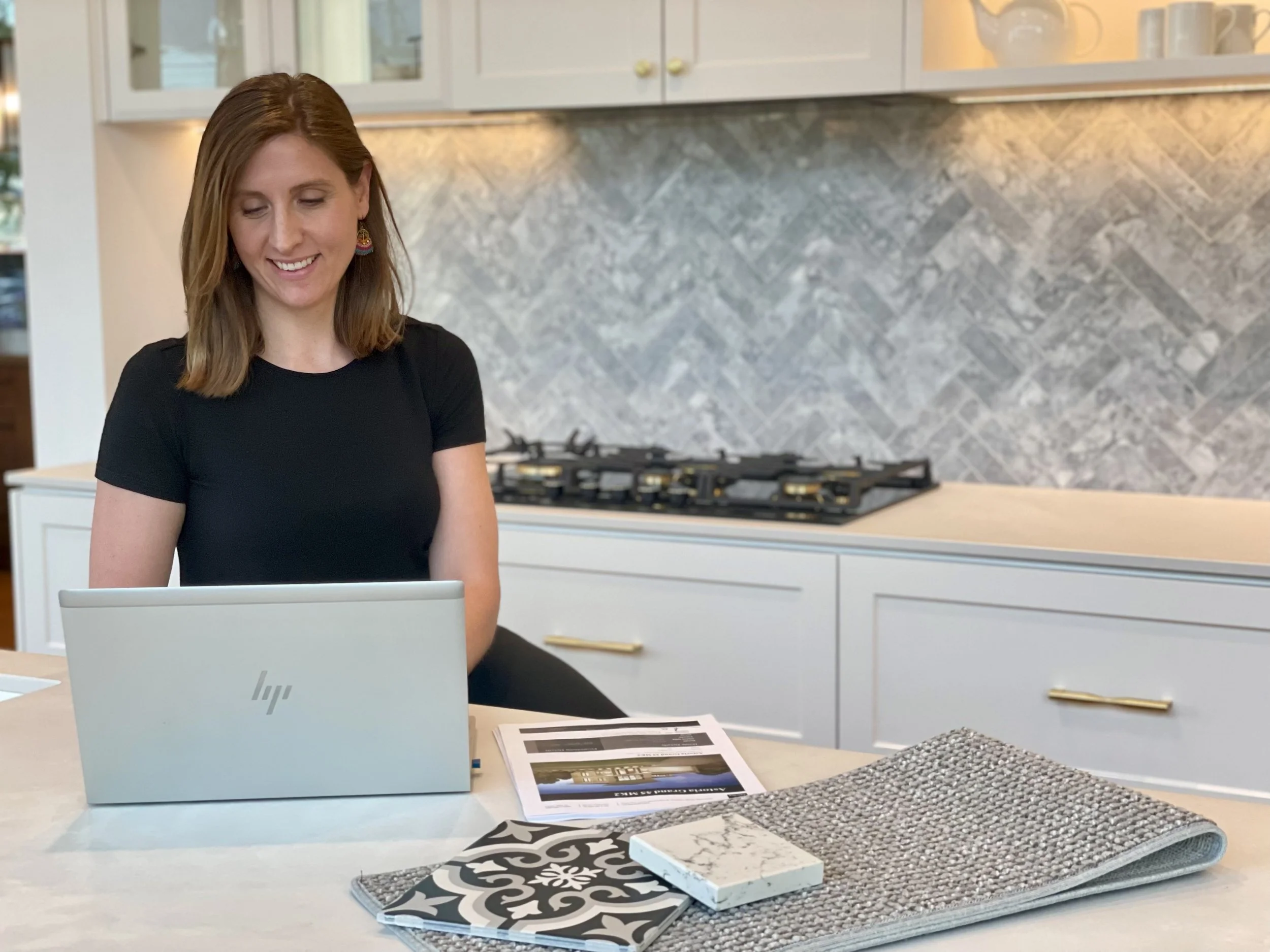 Tahlia Belcher of Light Design Co. working on a laptop at a kitchen bench with tile and stone samples