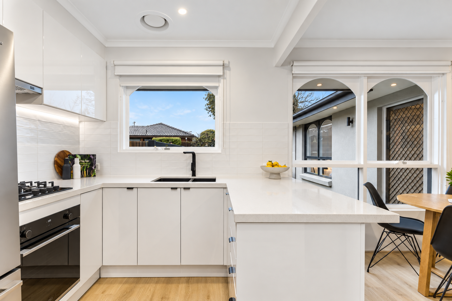 Centre project L-shaped white kitchen with black tapware, under-bench oven and arched window