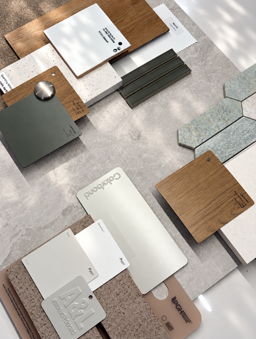 Material samples for a selections consultation: sage laminate, oak, terrazzo, green fluted tiles and a pale green stone mosaic with Colorbond and paint swatches