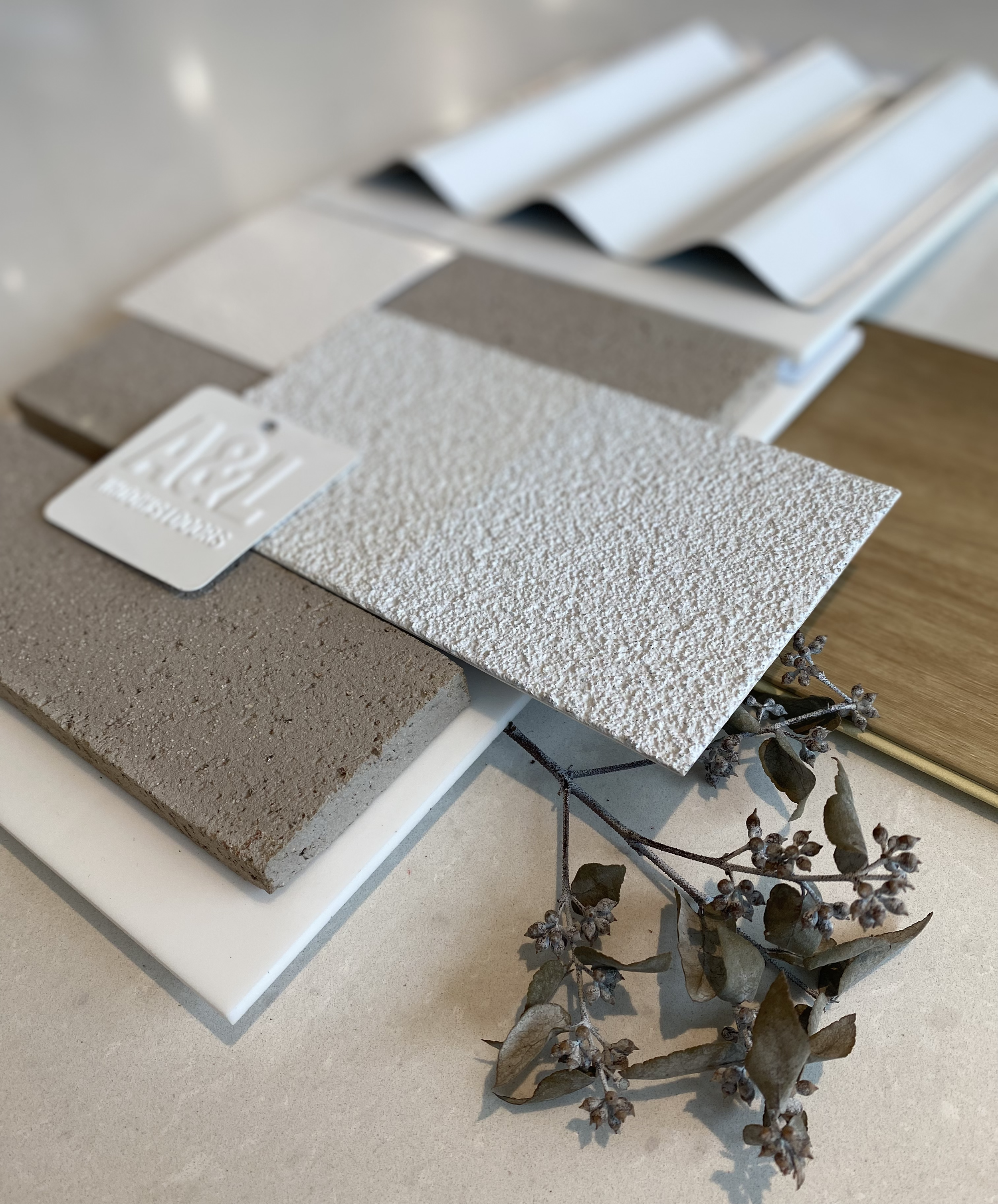 Exterior flatlay of textured white render, grey concrete-look panel, white fluted cladding and dried eucalyptus