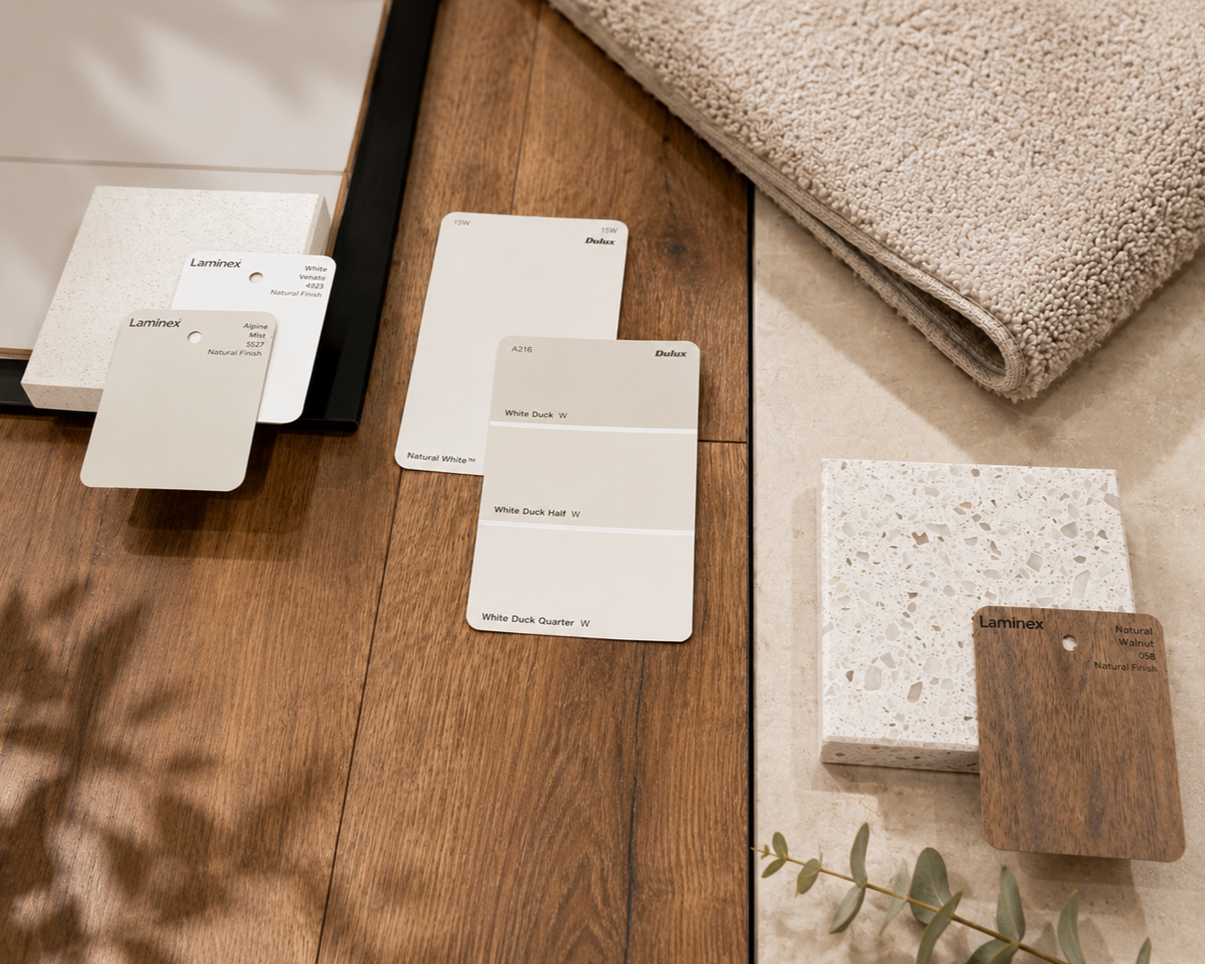 Neutral paint swatches, terrazzo and timber samples laid on oak flooring beside a soft carpet