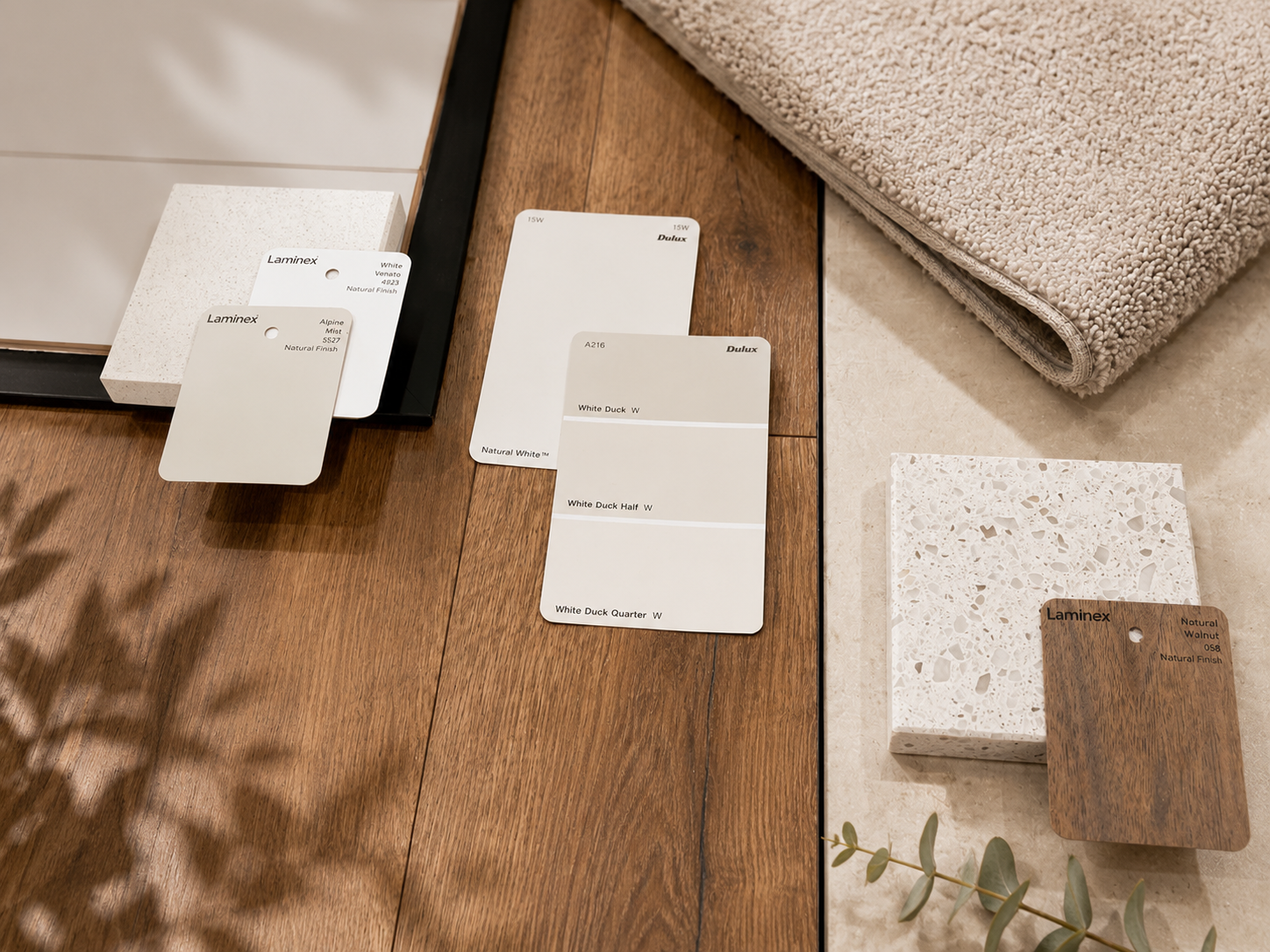 Flatlay of neutral paint swatches, terrazzo and timber laminate with soft carpet on dark oak flooring