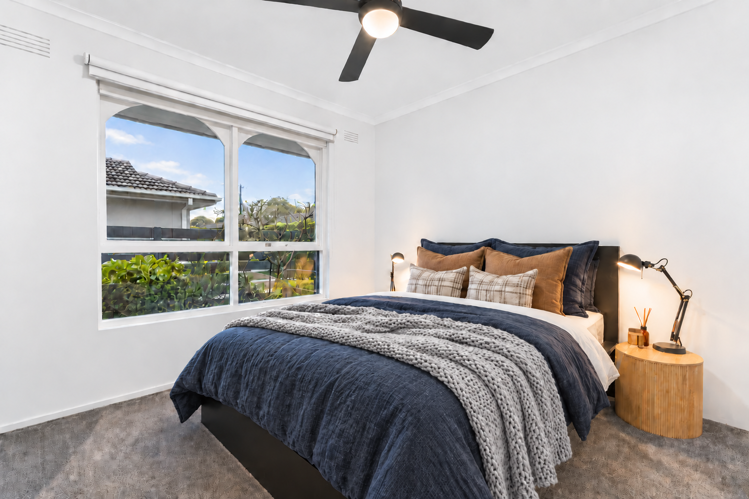 Centre project bedroom with navy quilt, textured throw, timber side table and black ceiling fan