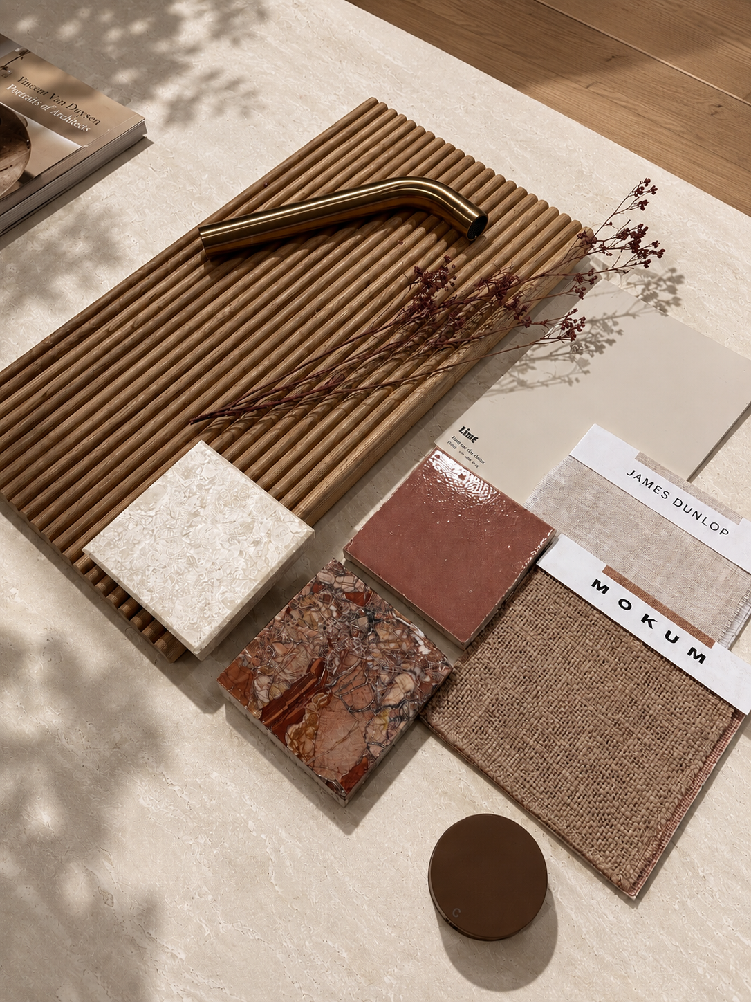 Warm earthy flatlay of terracotta tile, red marble, timber fluted panel, woven fabric and dried grasses