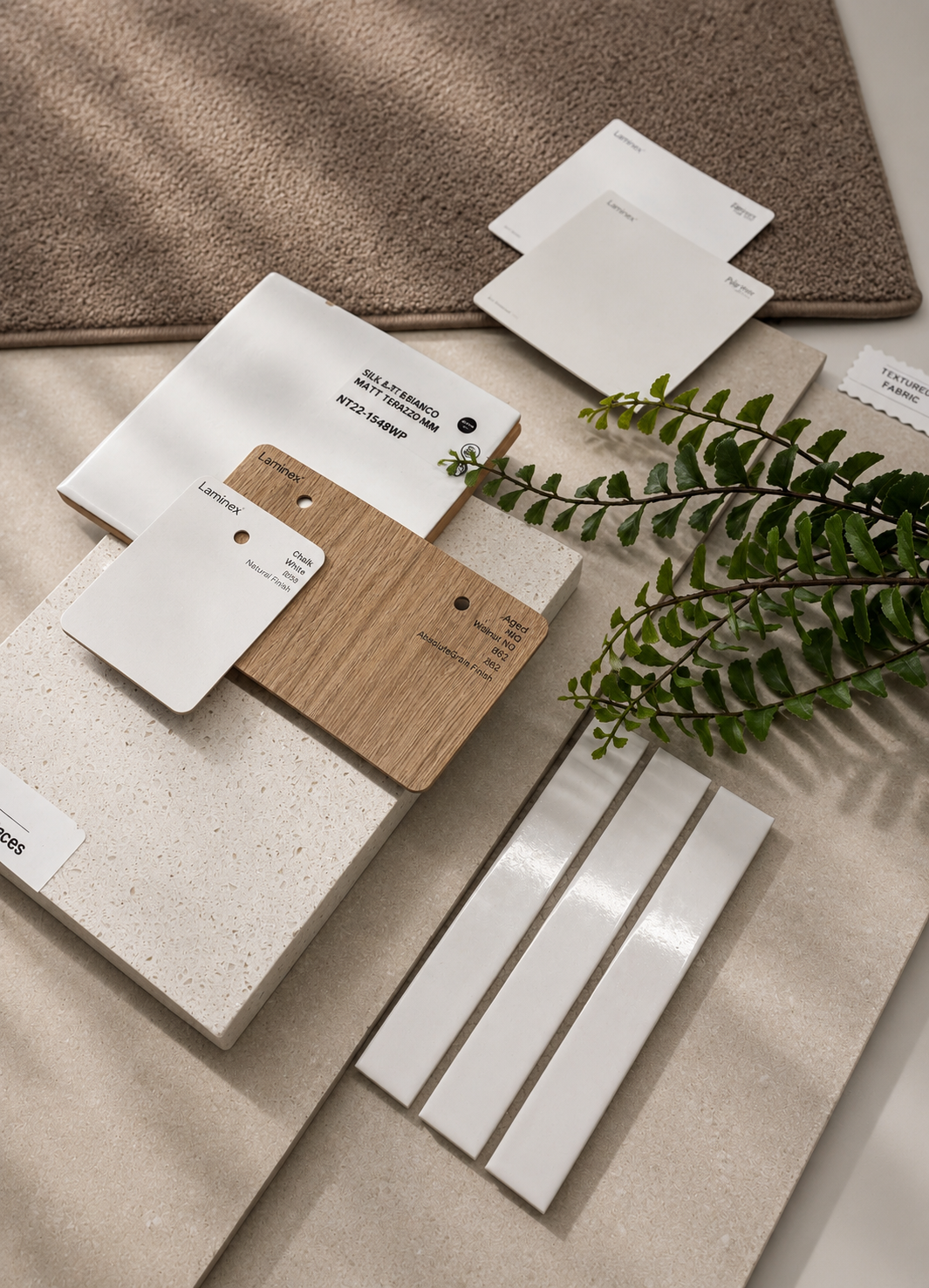 Flatlay of carpet, white stone, timber laminate and white gloss subway tiles with a fern sprig