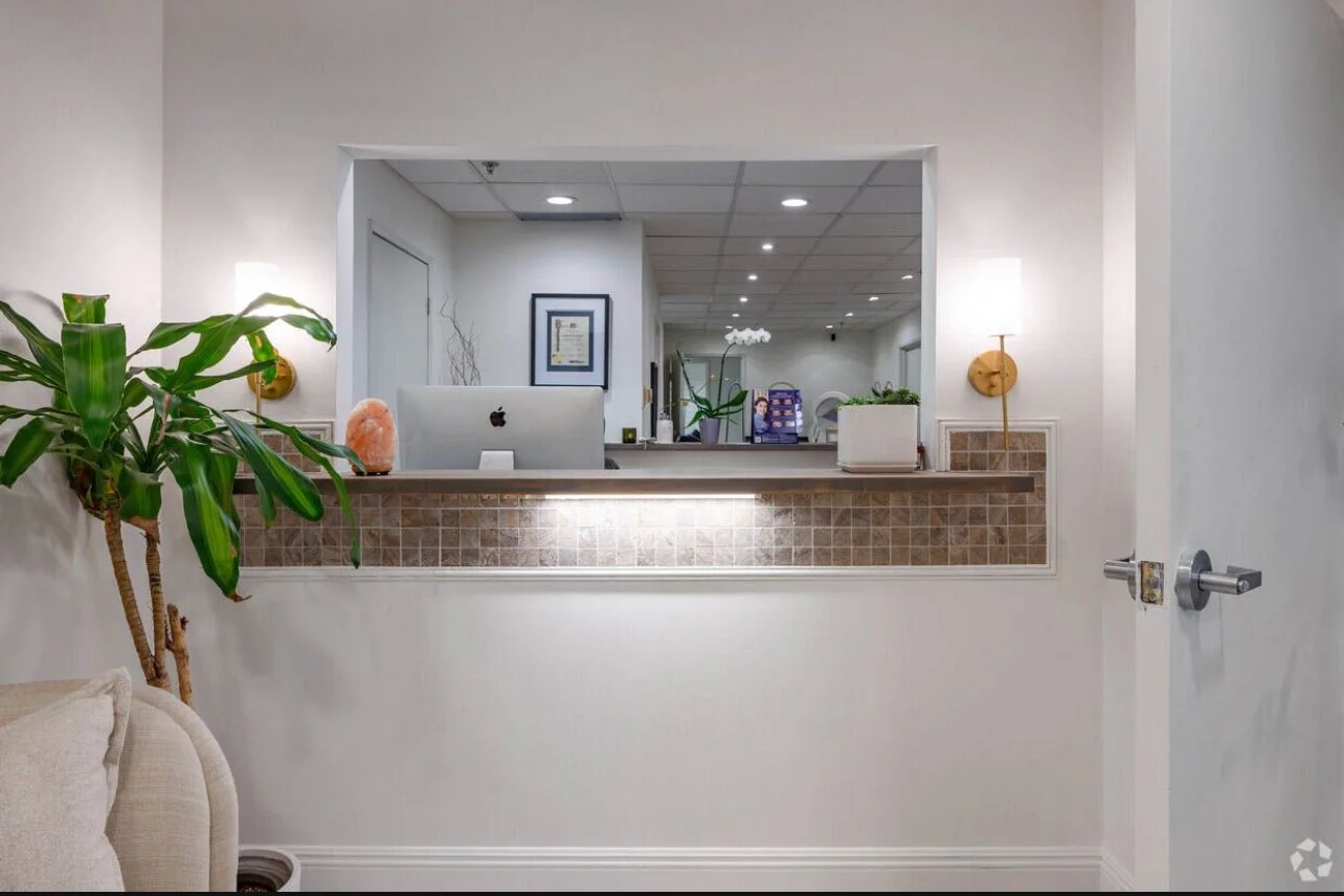 Reception desk with a computer, plants, and lamps in a modern office or clinic