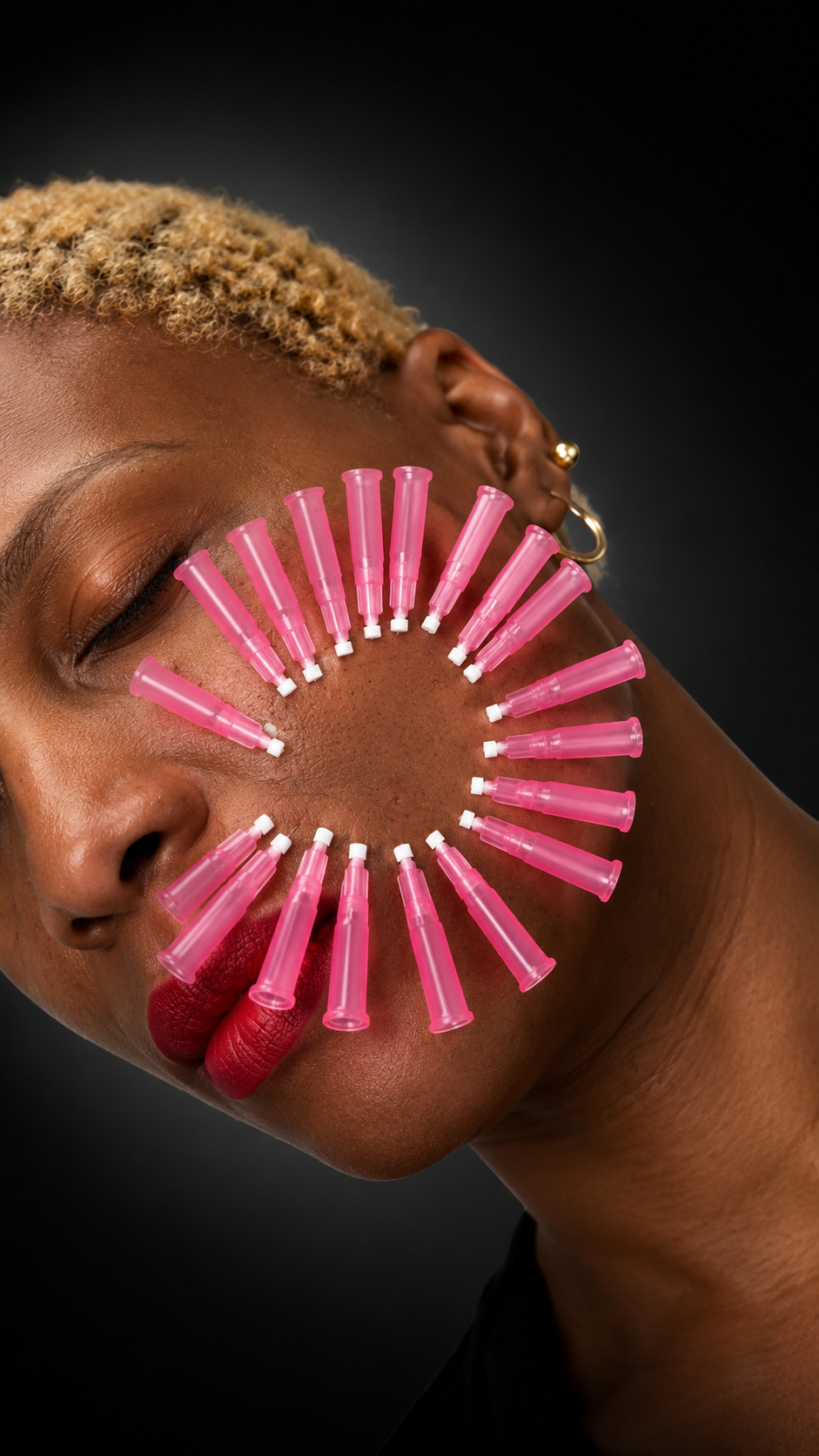 A woman with short blonde hair has pink nasal spray bottles arranged in a circle on her face, covering her right cheek and part of her lips, set against a black background.