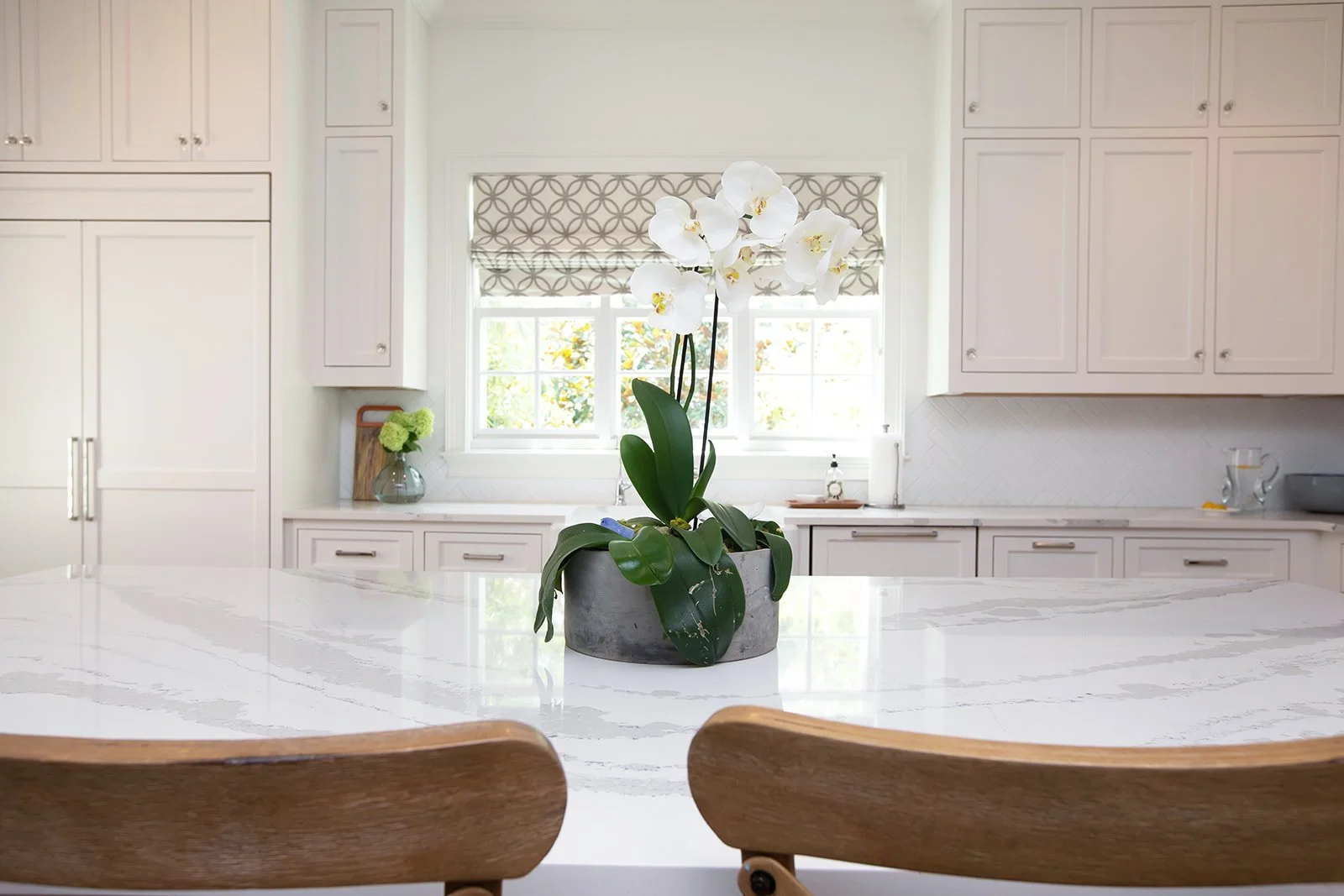Modern kitchen with white cabinets, a marble island countertop, and a white orchid centerpiece.