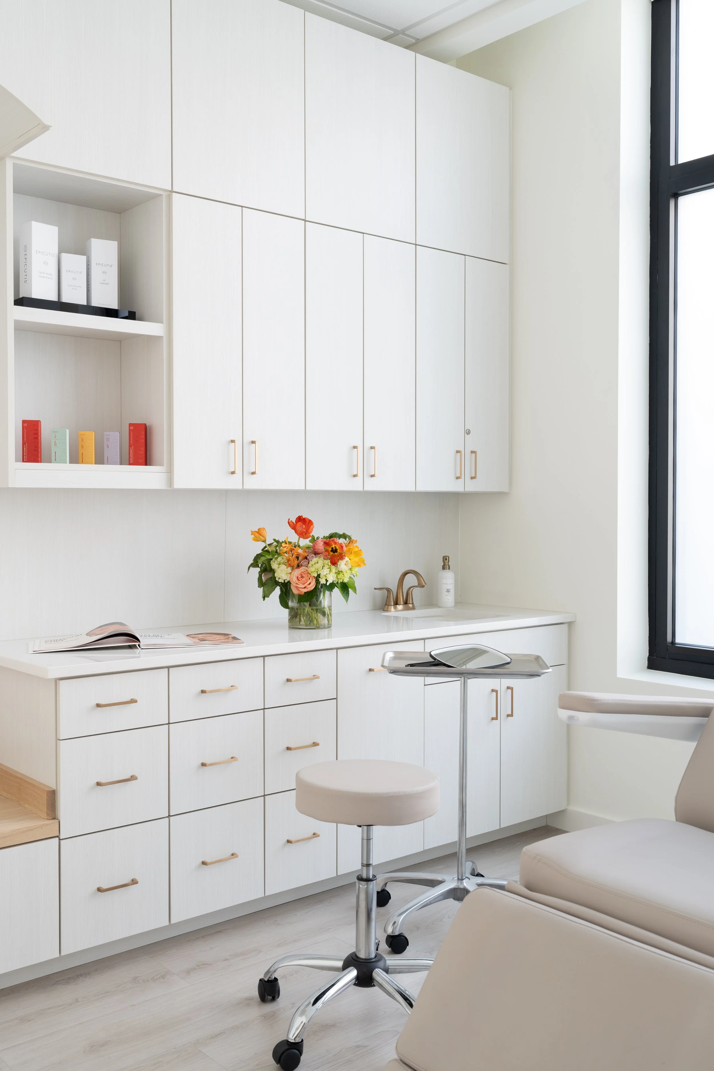 Modern medical or dental office with white cabinets, a flower arrangement, a small sink, and a stool.