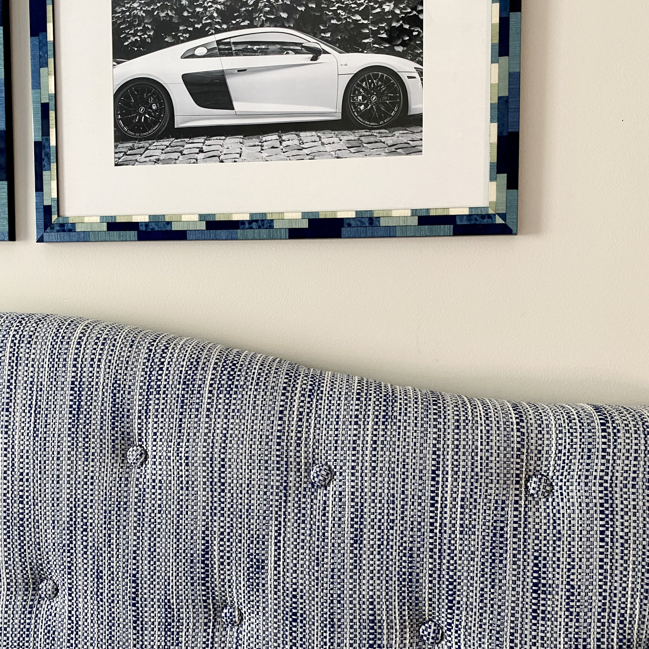 Framed black and white photo of a luxury sports car above a blue and white upholstered headboard.