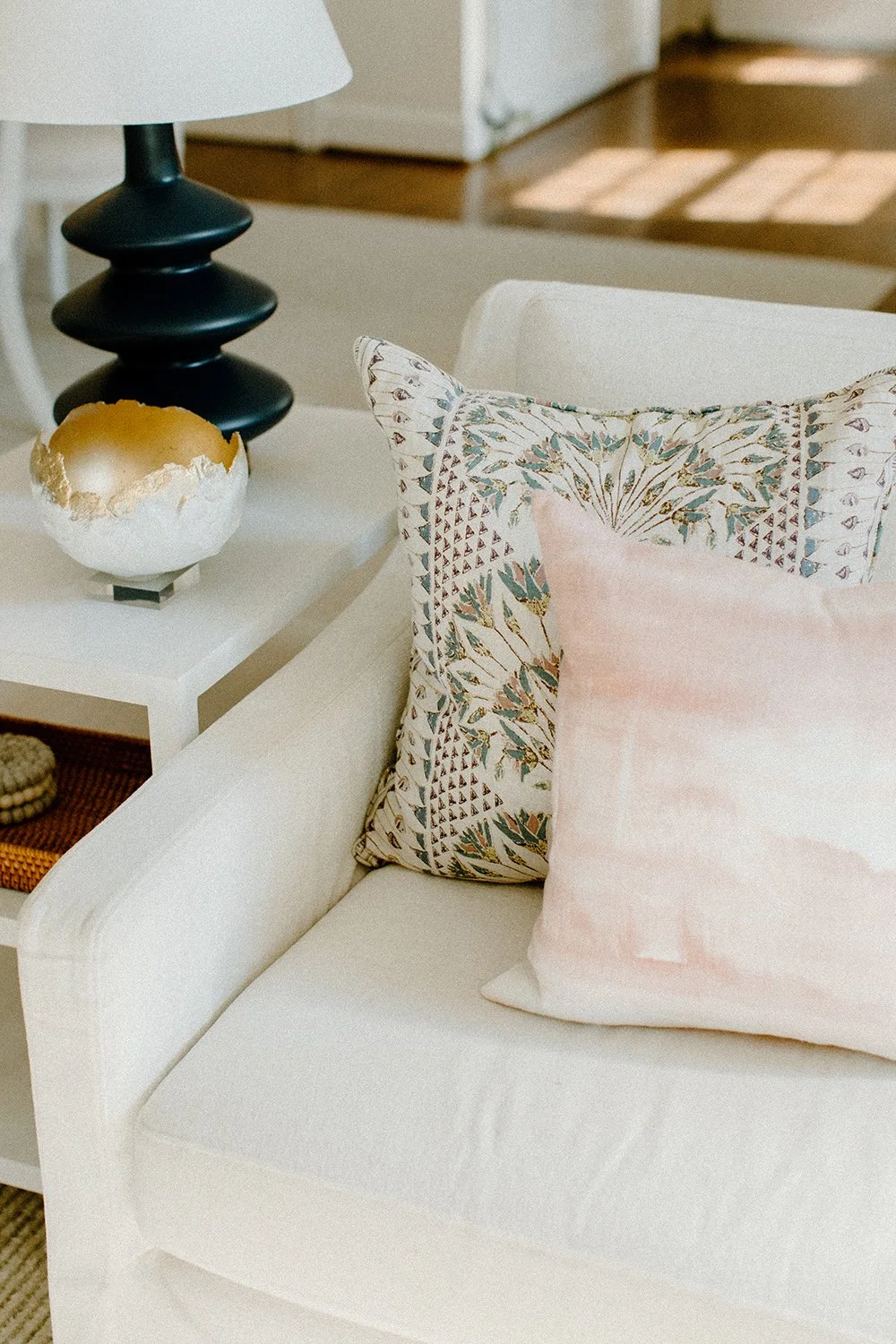 White armchair with patterned and solid decorative pillows, black lamp, and a decorative bowl on a side table.