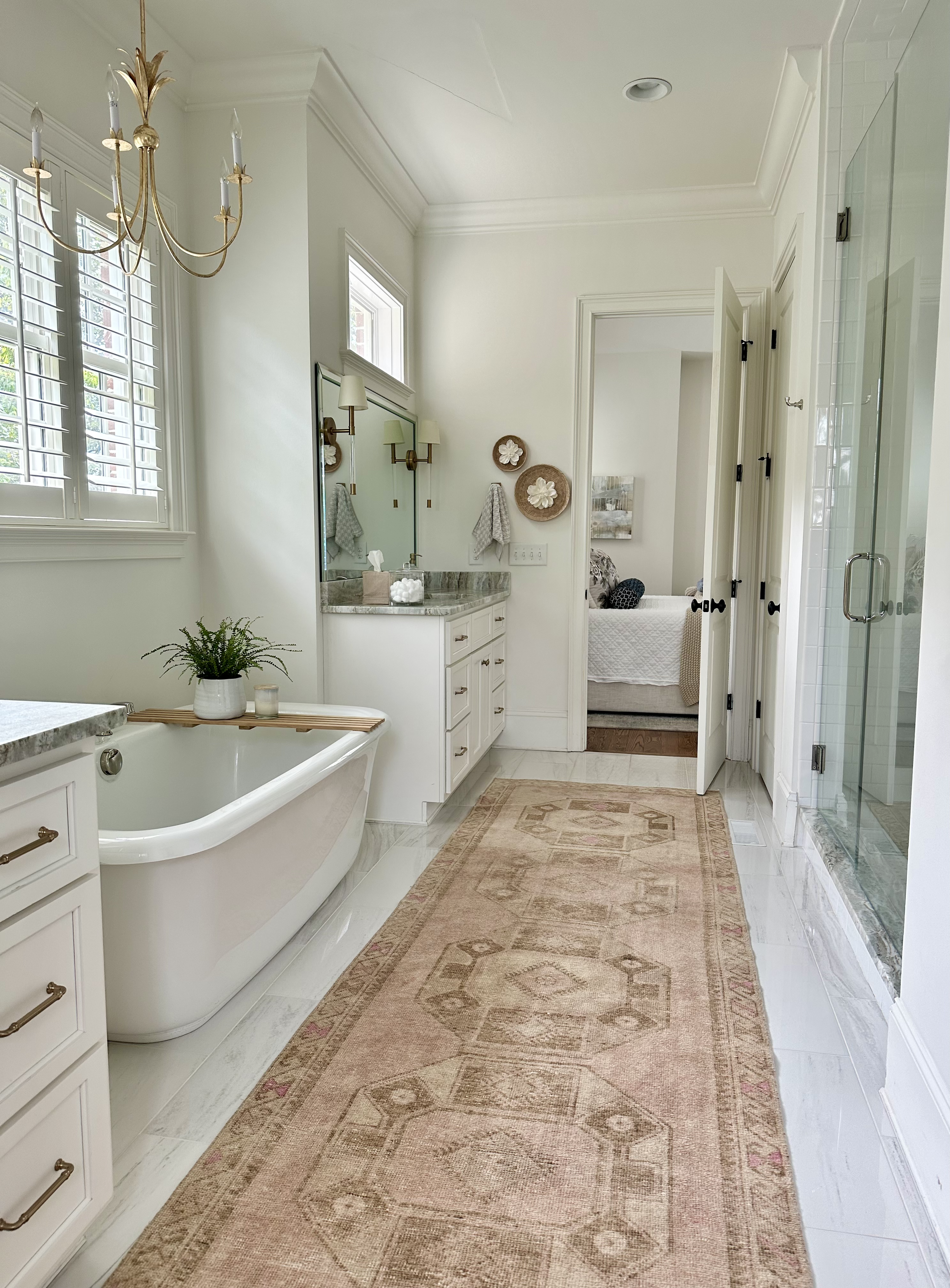 Elegant bathroom with freestanding bathtub, patterned rug, chandelier, and double vanity with mirrors.