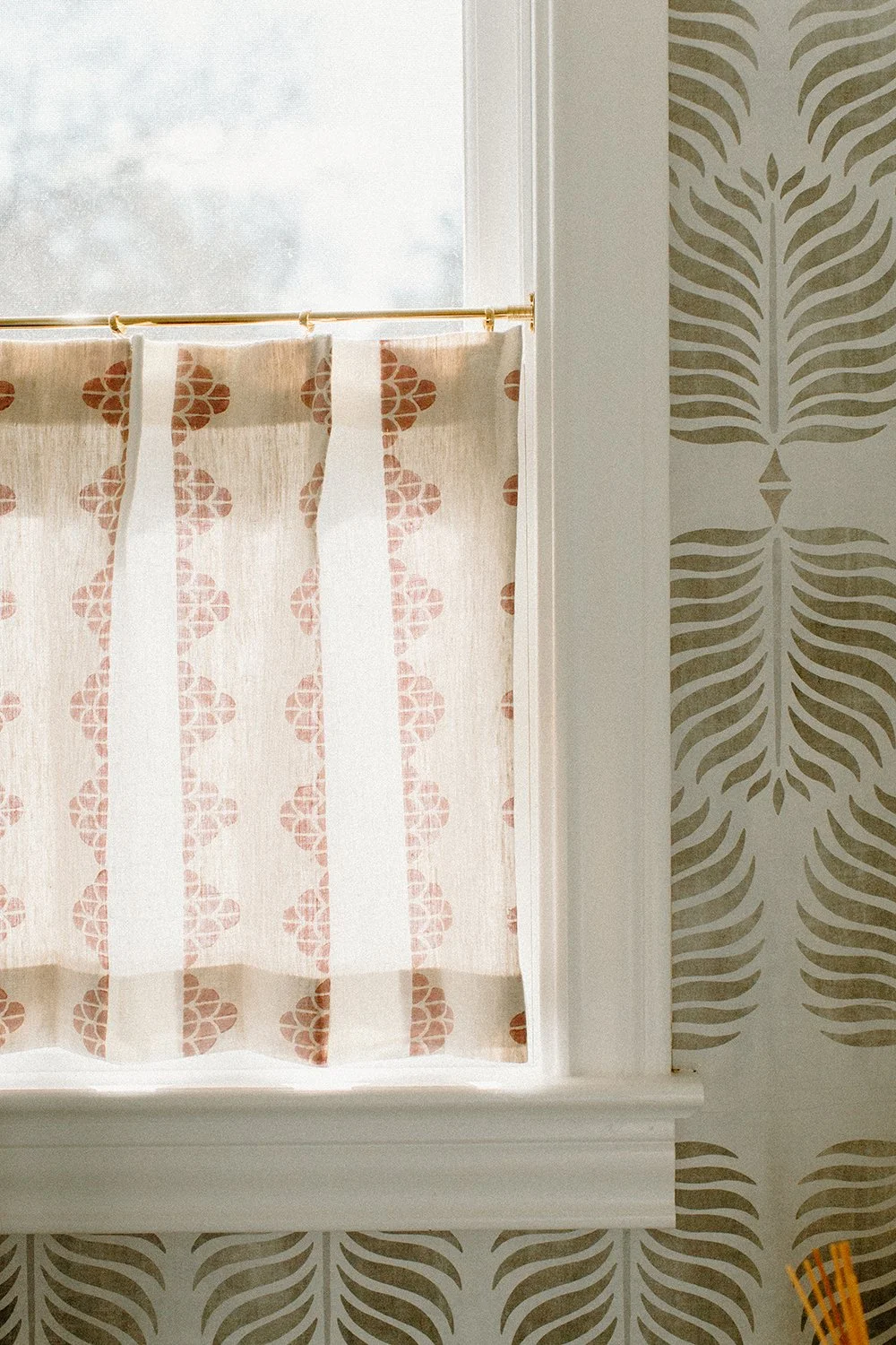 Window with curtain featuring red geometric pattern, surrounded by decorative wallpaper with leaf design.