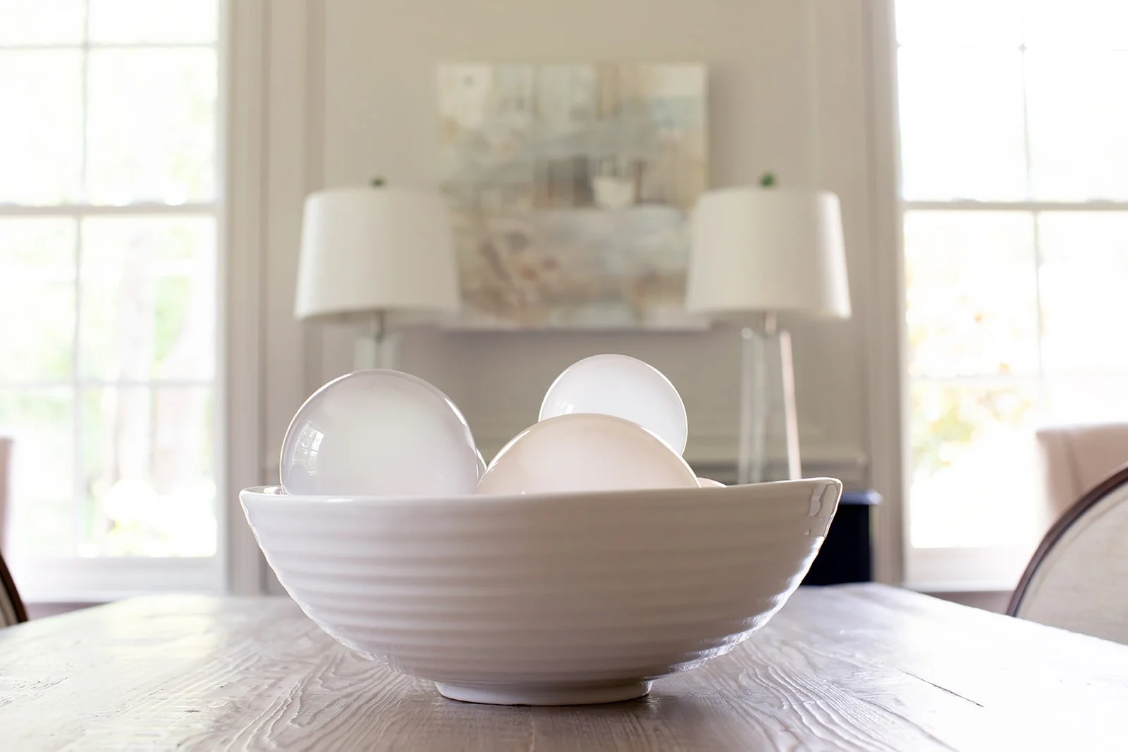 White ceramic bowl with glass globes on wooden table, modern decor.