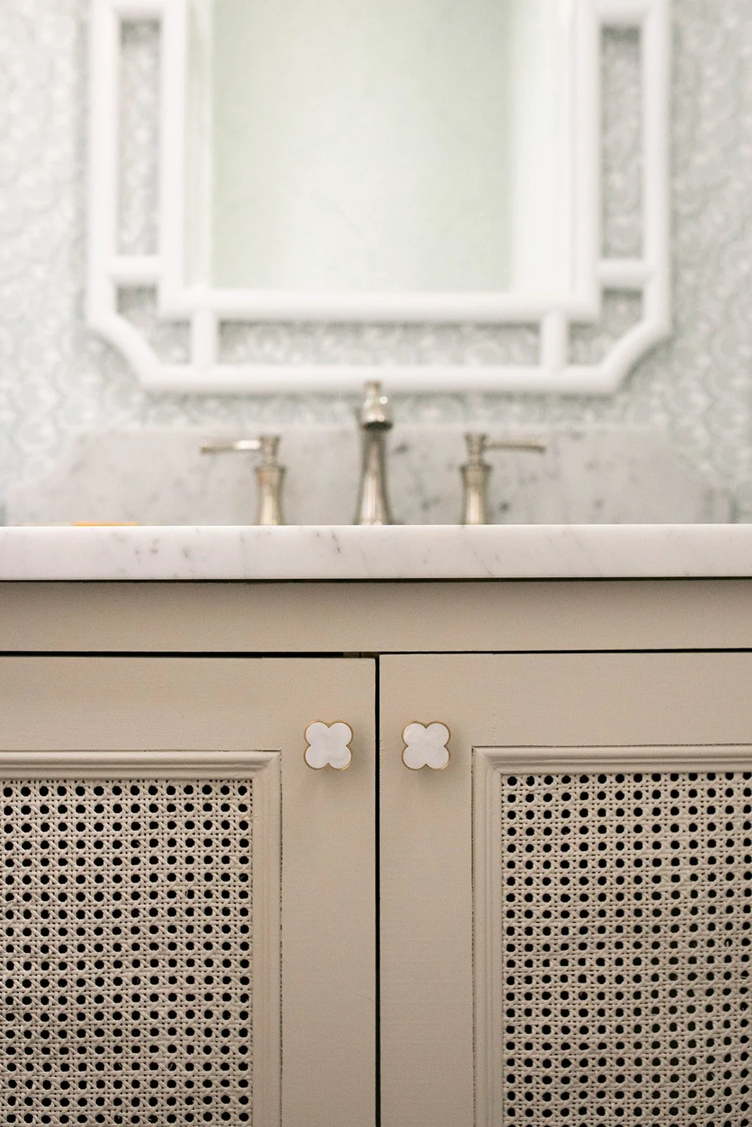 Bathroom vanity with wicker paneling and white marble countertop, featuring decorative knobs and chrome faucet, with a white-framed mirror in the background.