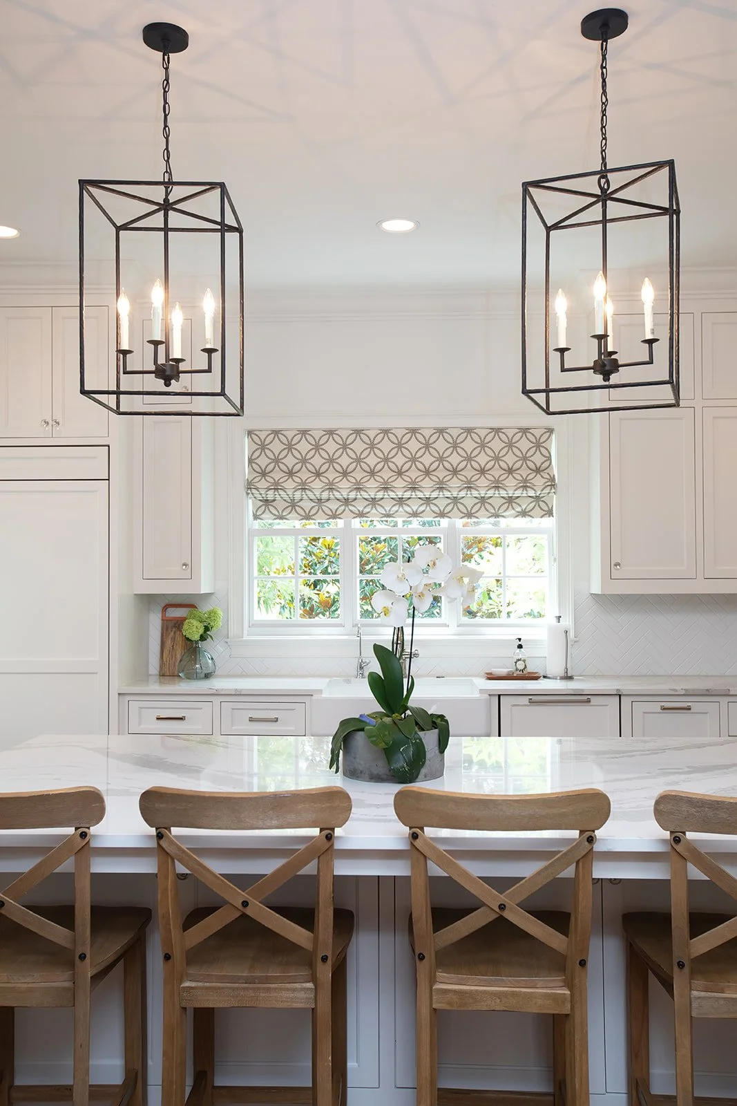 Modern kitchen with pendant lights, white cabinetry, and a marble countertop island with wooden stools.