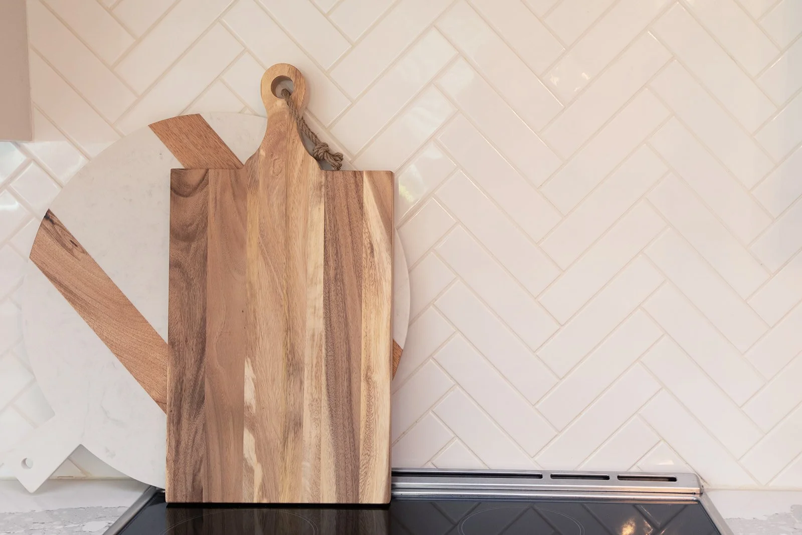Wooden cutting board leaning against white herringbone tile backsplash.