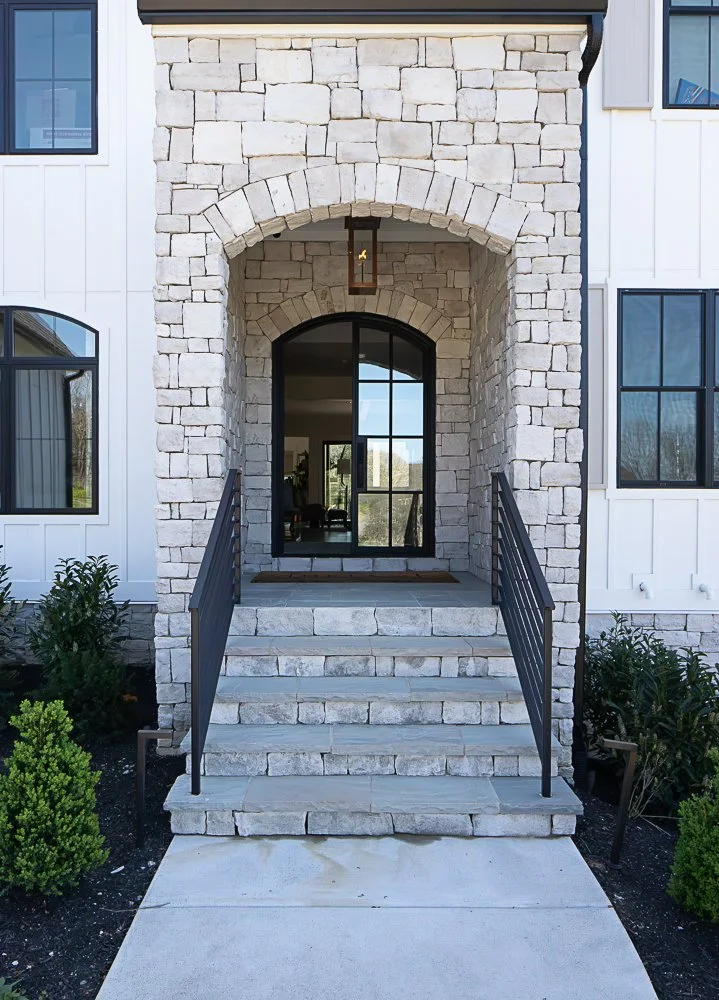 Stone porch with steps leading to an arched entrance in a modern house.