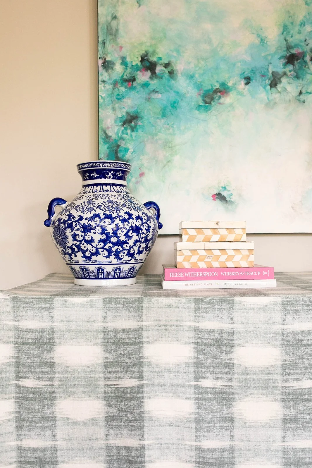 Blue and white ceramic vase on table with books, in front of abstract painting.