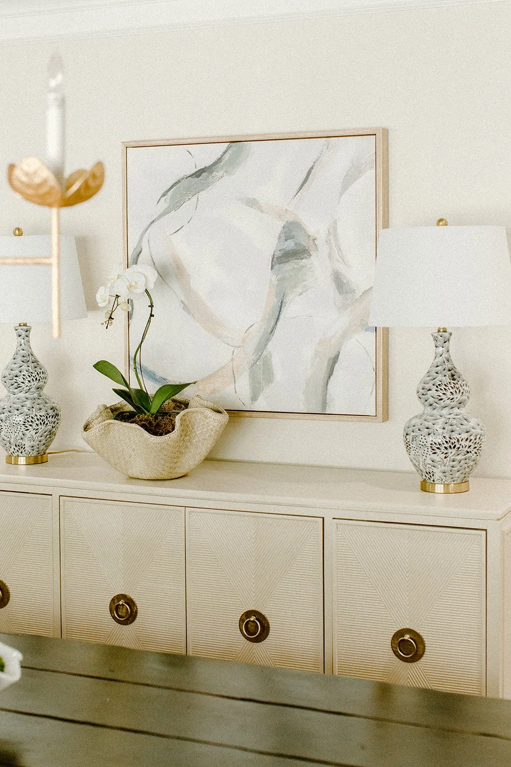 Interior decor with abstract art, orchid plant, decorative lamps, and sideboard.