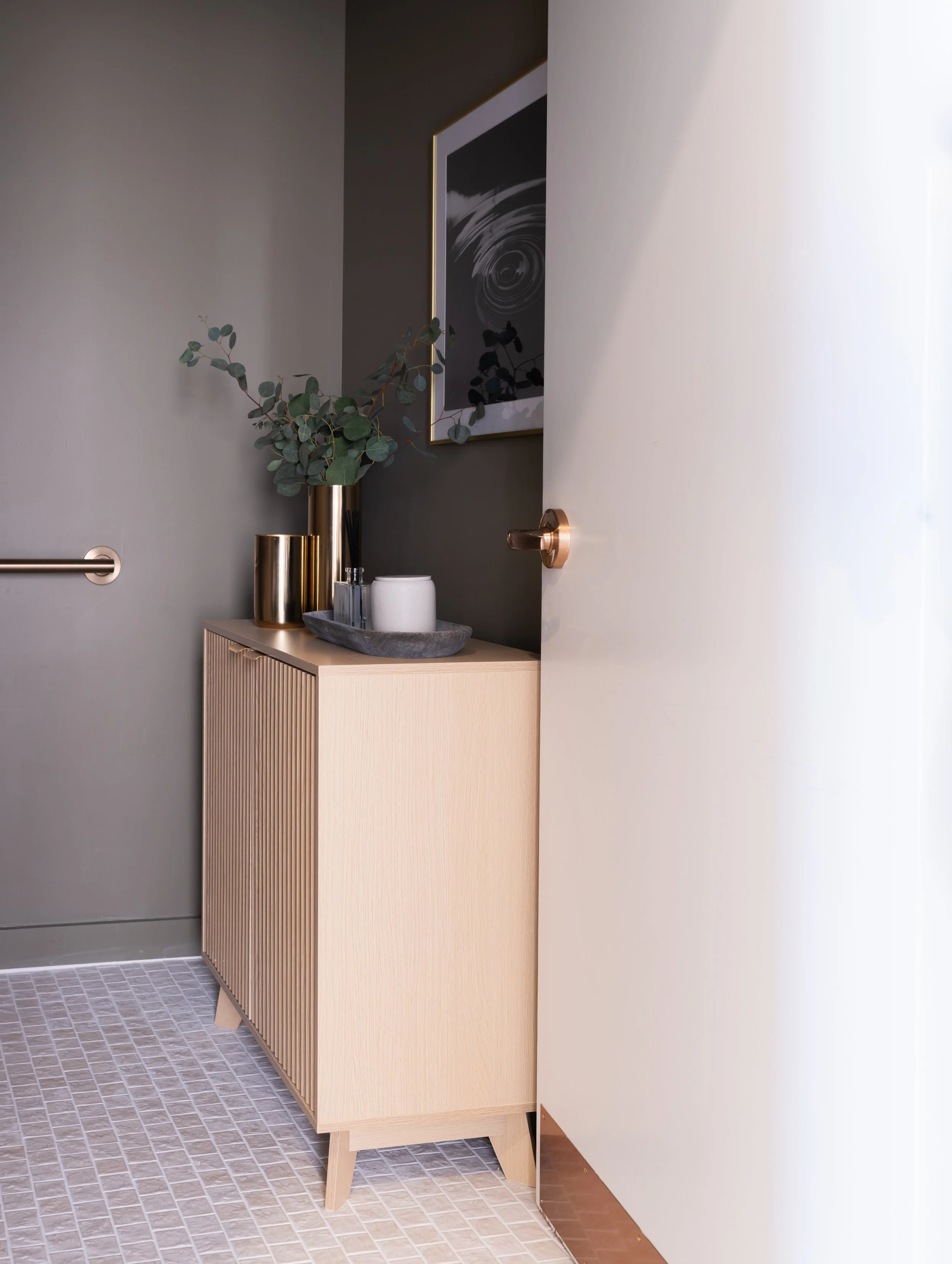 Interior of a modern room with a wooden cabinet, decorative vases, a tray with a candle, a framed abstract wall art, and a door partially open.