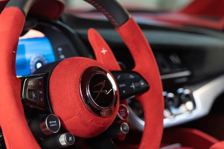 Volante di un'auto sportiva con rivestimento in alcantara rosso e controlli integrati.