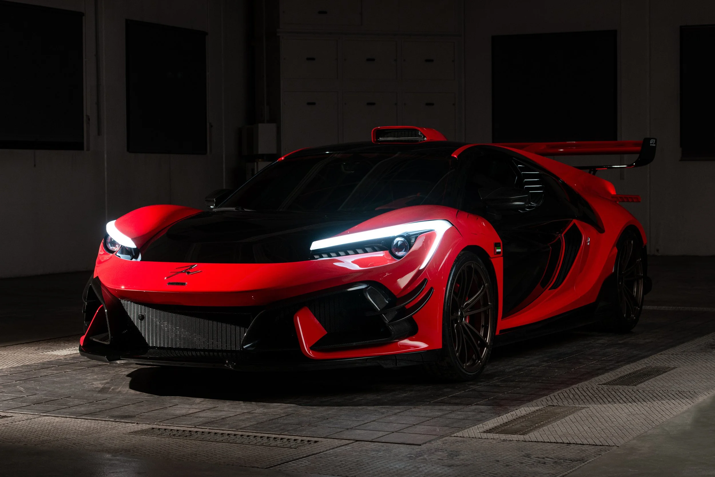 Auto sportiva rossa e nera in garage, fari accesi, aliscafo posteriore grande.