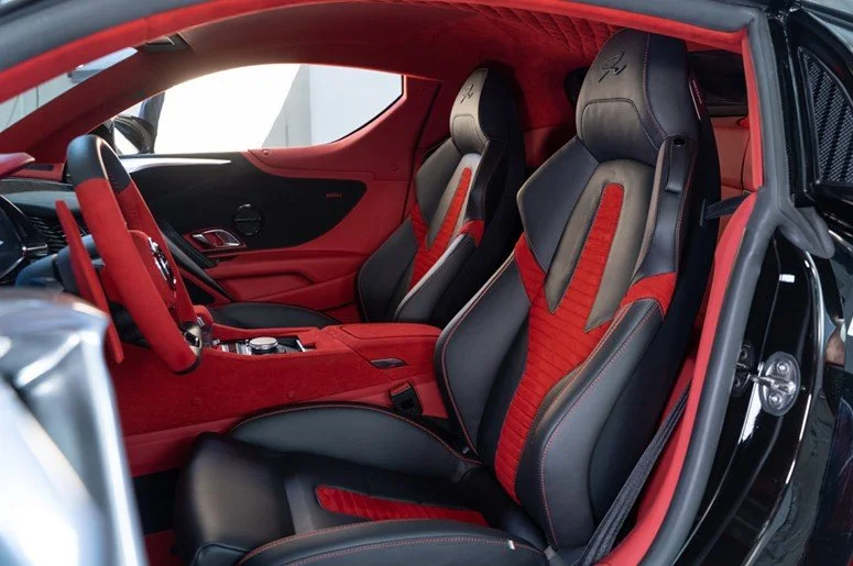 Interni di un'auto sportiva con sedili in pelle nera e rossa, volante coordinato e finiture di lusso.