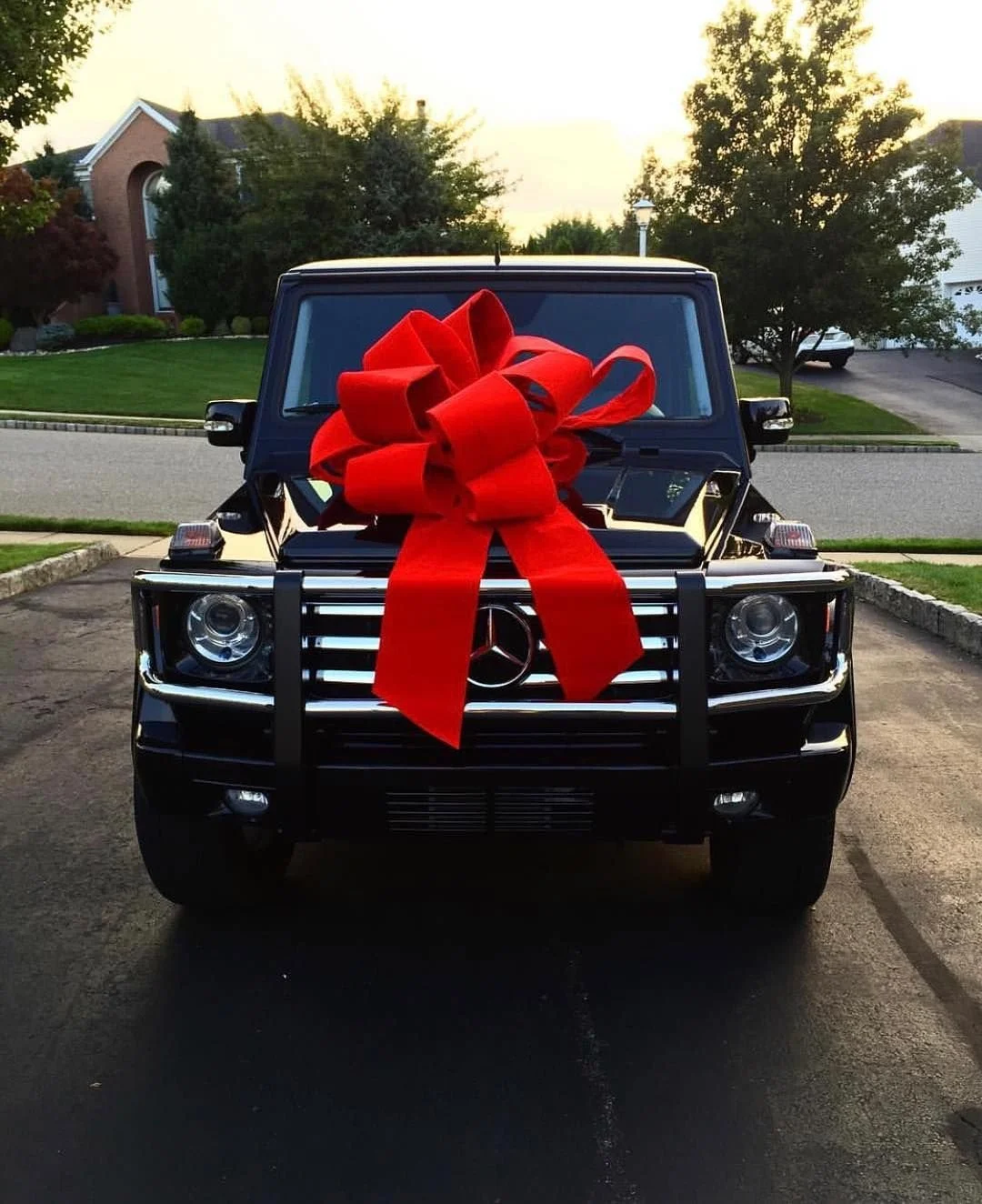 Un SUV Mercedes-Benz con un grande fiocco rosso sul cofano, parcheggiato in un vialetto.