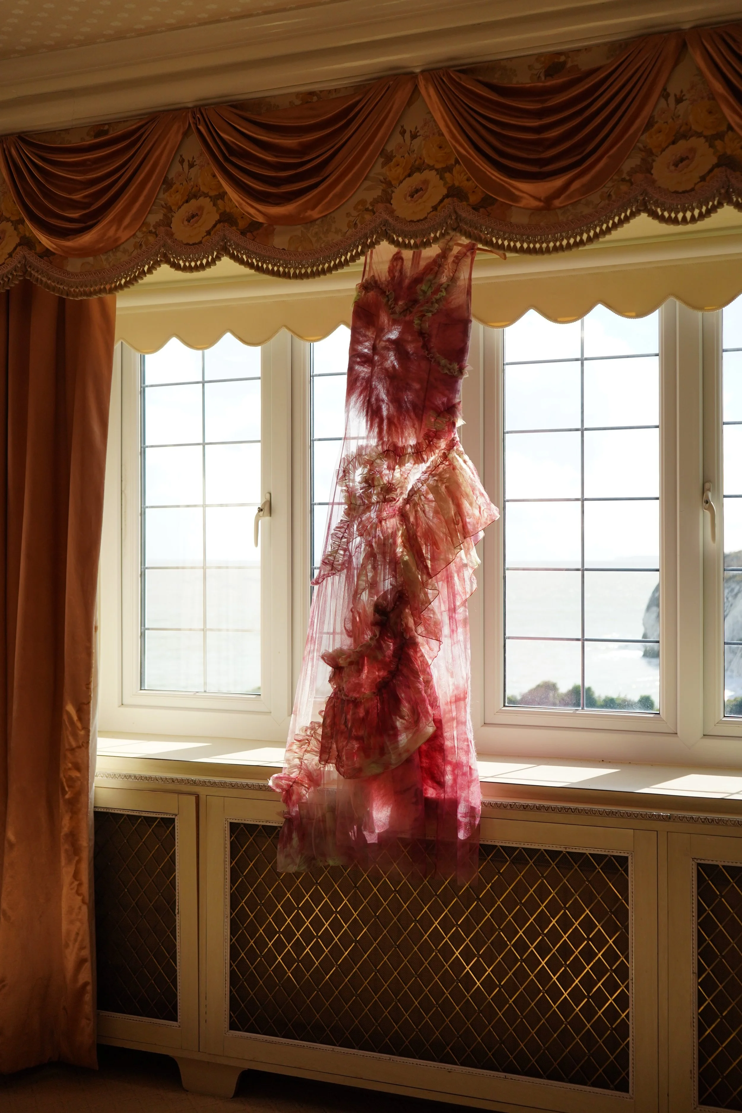 Flourishing Dress by Clara Pinto hanging by window – showing full length silhouette and layered pink tulle with green frills